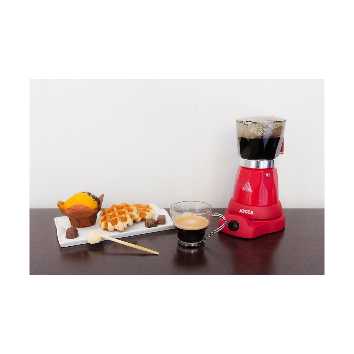 Caffettiera rossa con waffle, dolci e tazza di caffè su un tavolo.