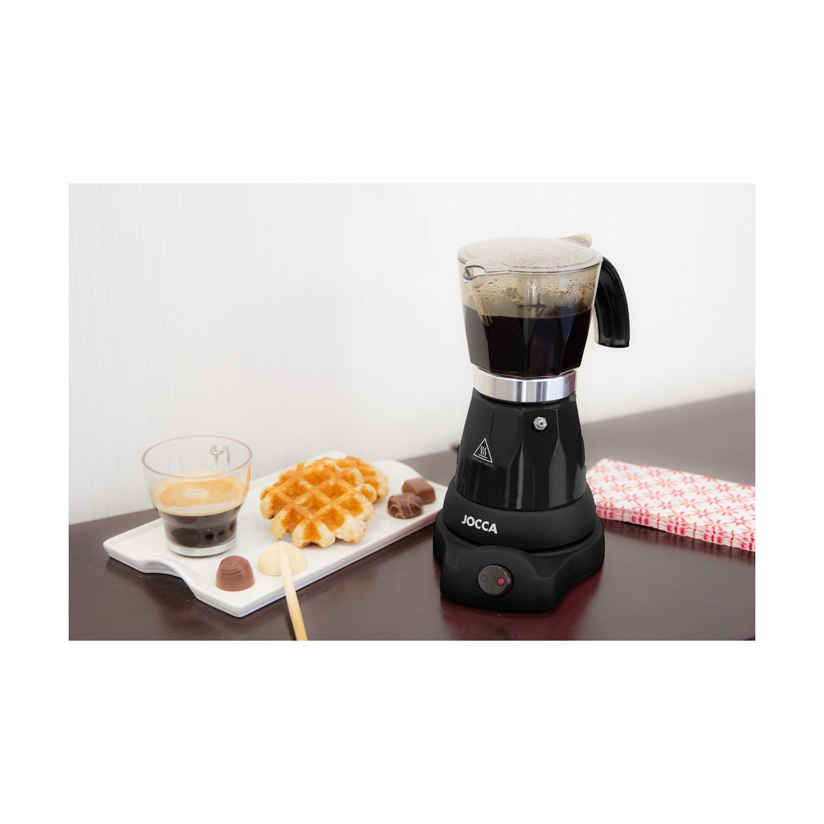 Una cafetera eléctrica negra, con gofres y café en una mesa.