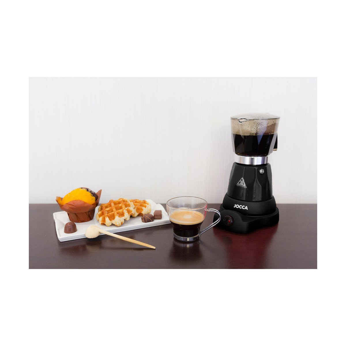Artículos de desayuno. Café negro, gofres, magdalena y chocolates en un plato blanco, cafetera espresso.