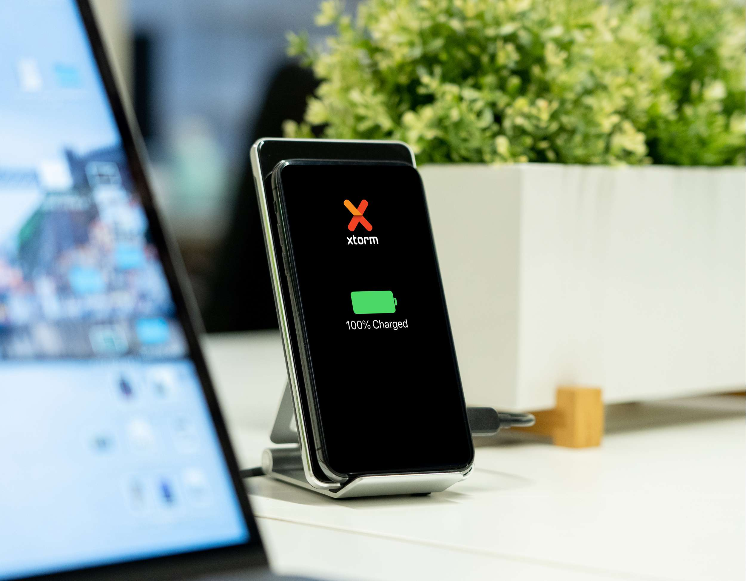 Schwarzes Telefon auf kabellosem Ladegerät mit grünem 100% Ladeanzeiger, Laptop links.