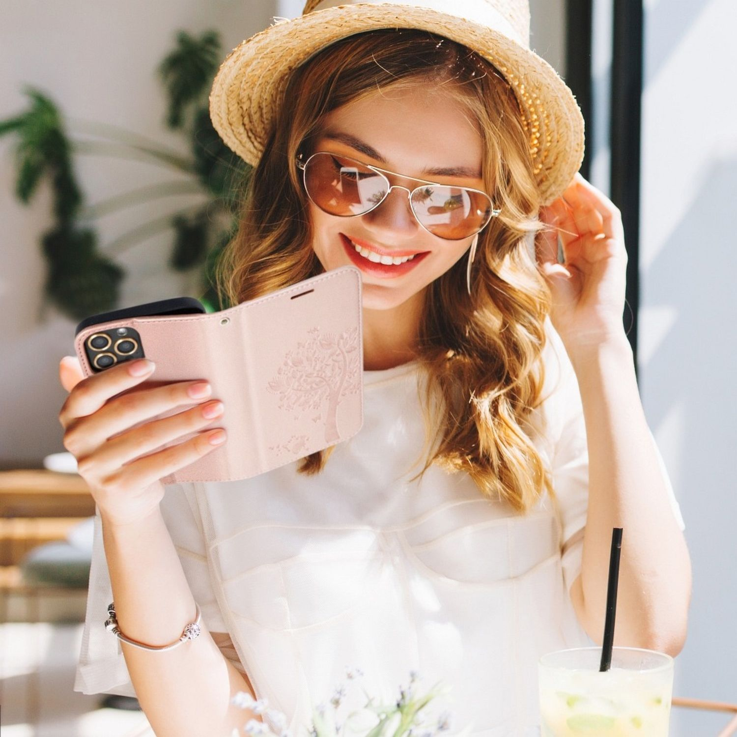 Eine Frau hält ein Telefon mit einer rosa Hülle, sitzt draußen in der Sonne.