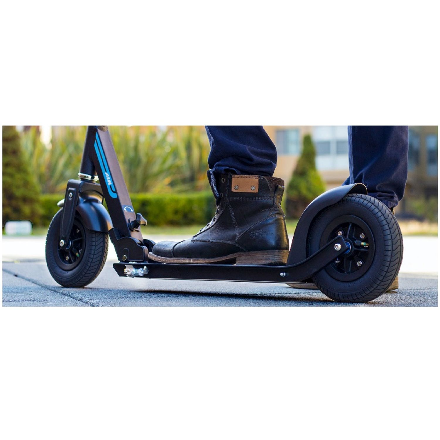 Une personne se tient sur un scooter électrique noir en extérieur, montrant les roues avant et arrière.