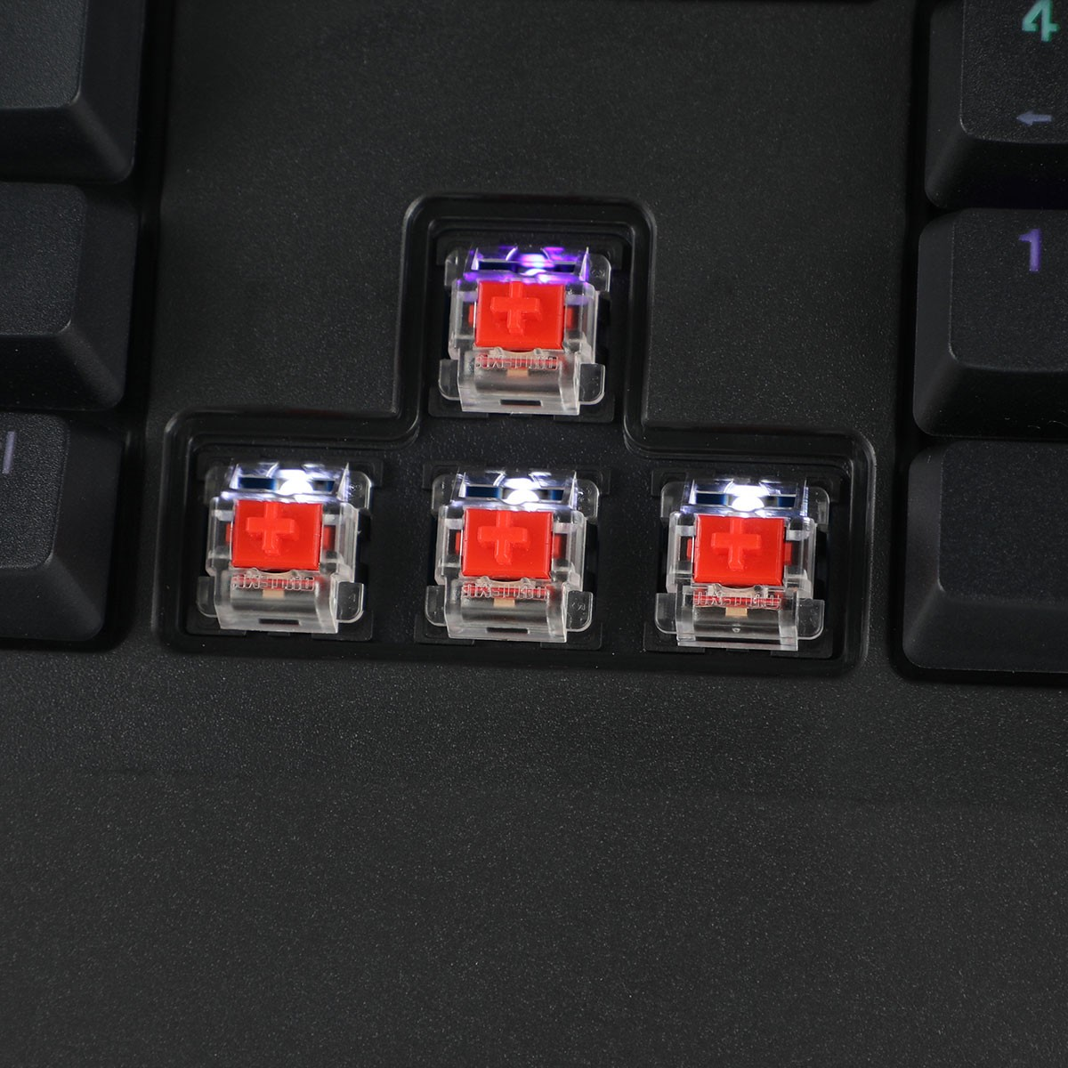 Primer plano de las teclas de un teclado mecánico. Tres interruptores rojos con teclas transparentes y cruces rojas.