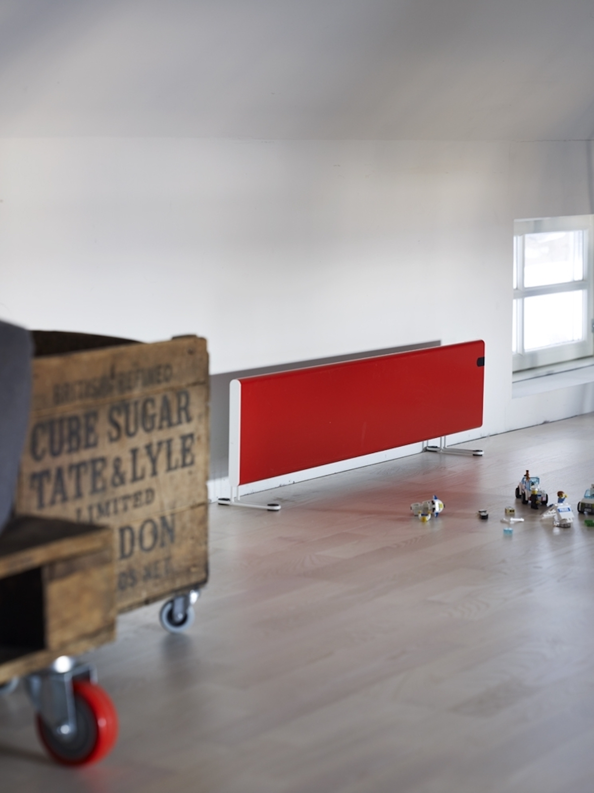 Termosifone rosso contro muro bianco. Scatola di legno a sinistra, giocattoli sul pavimento.