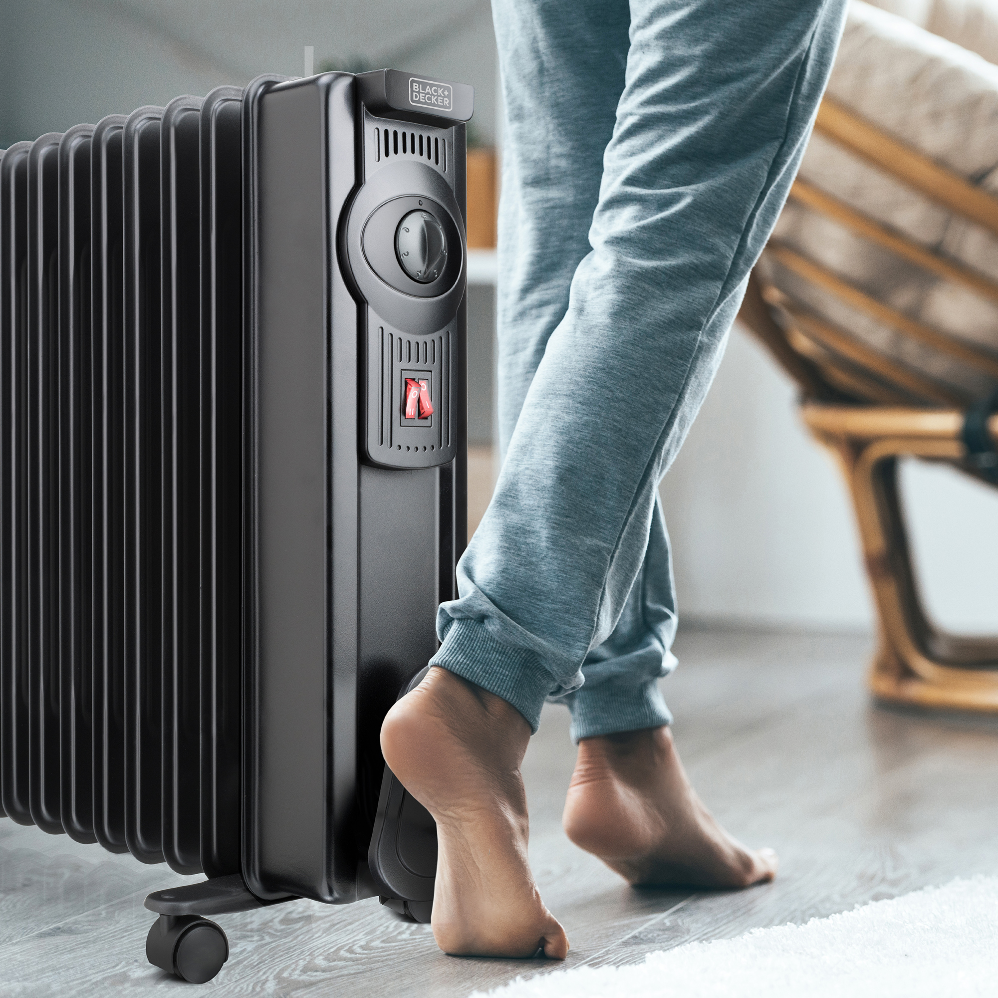 Osoba stojąca obok czarnego grzejnika. Widoczne bose stopy osoby.