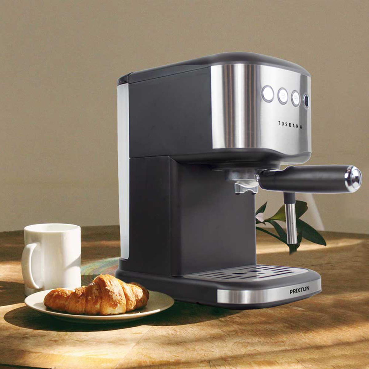 Ekspres do kawy z rogalikiem i kubkiem na stole. Maszyna jest czarna i srebrna.
