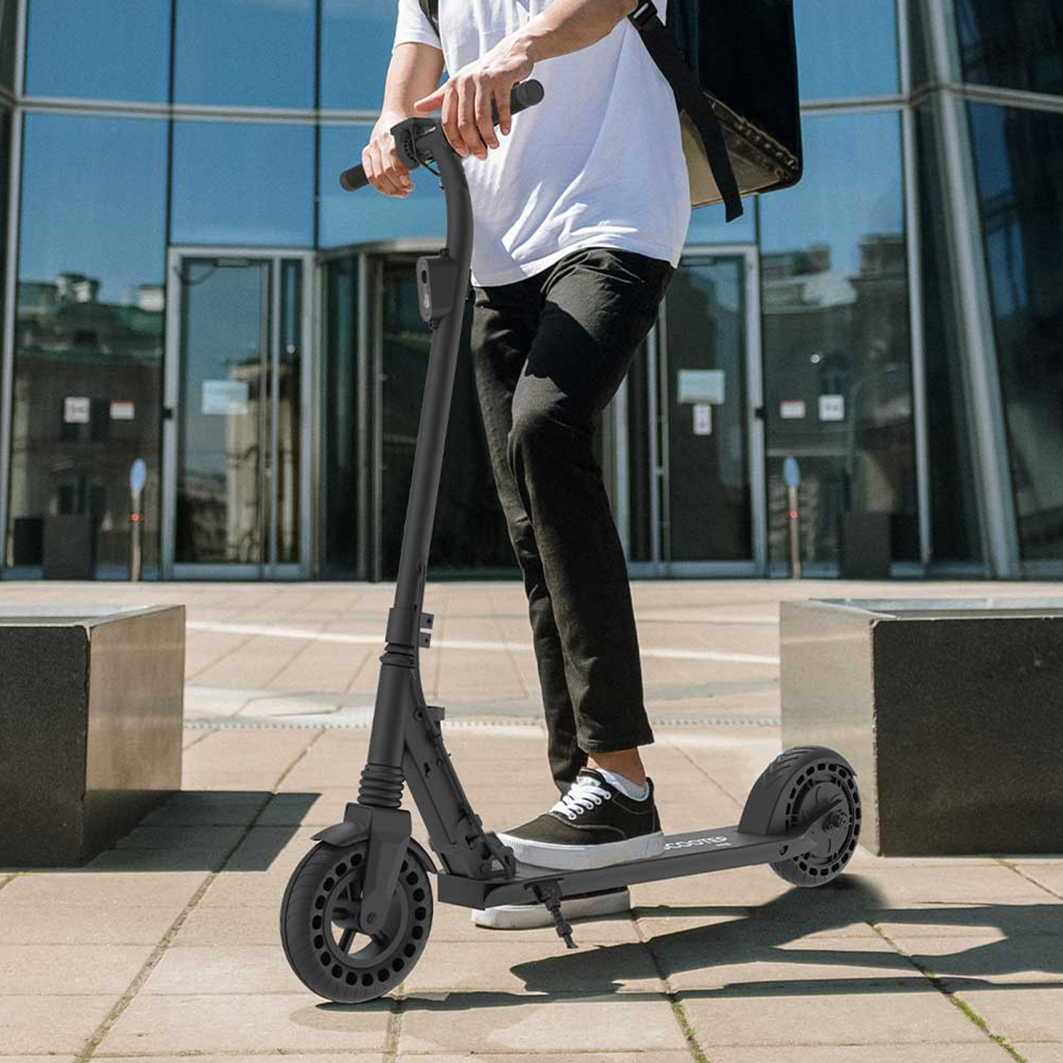 Persona su un monopattino elettrico nero davanti a un edificio moderno.