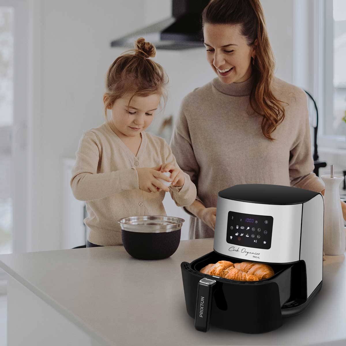 Una donna e una bambina cucinano, con una friggitrice ad aria in primo piano e la cucina sullo sfondo.