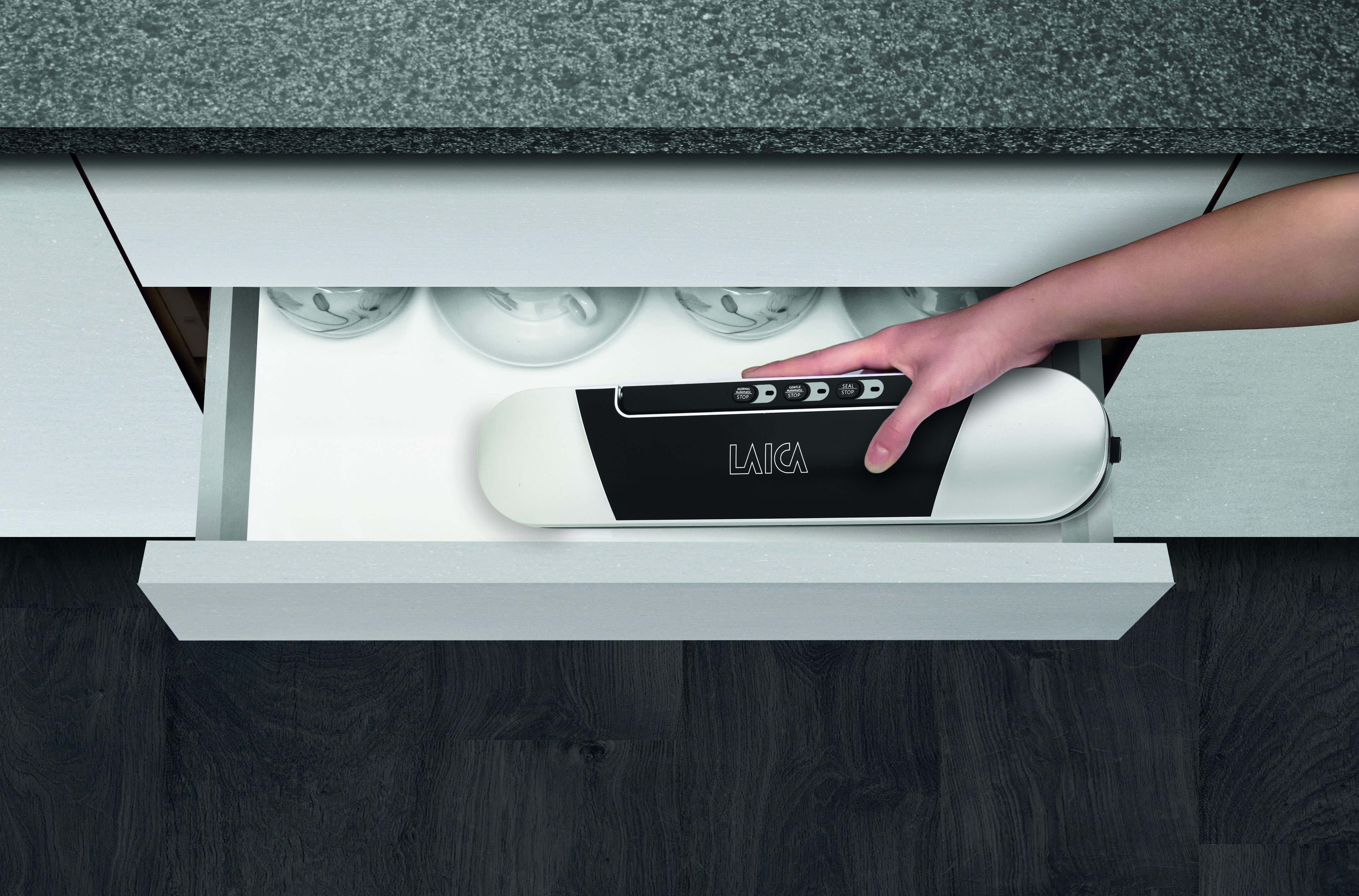 Ręka sięga do szuflady, aby chwycić biało-czarną zgrzewarkę próżniową. Szuflada jest otwarta.