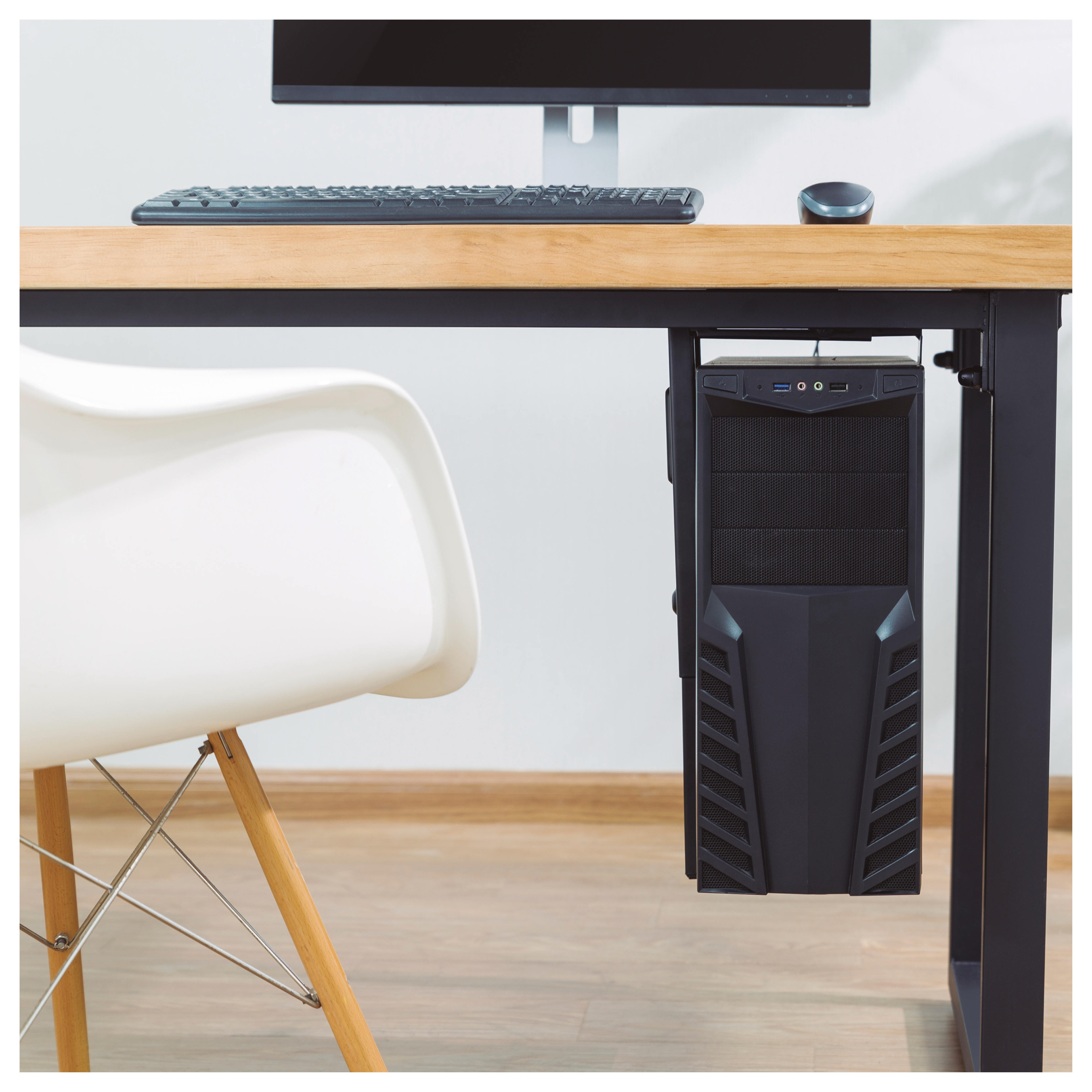 Una carcasa de computadora negra colgando debajo de un escritorio de madera, con una silla blanca cerca.