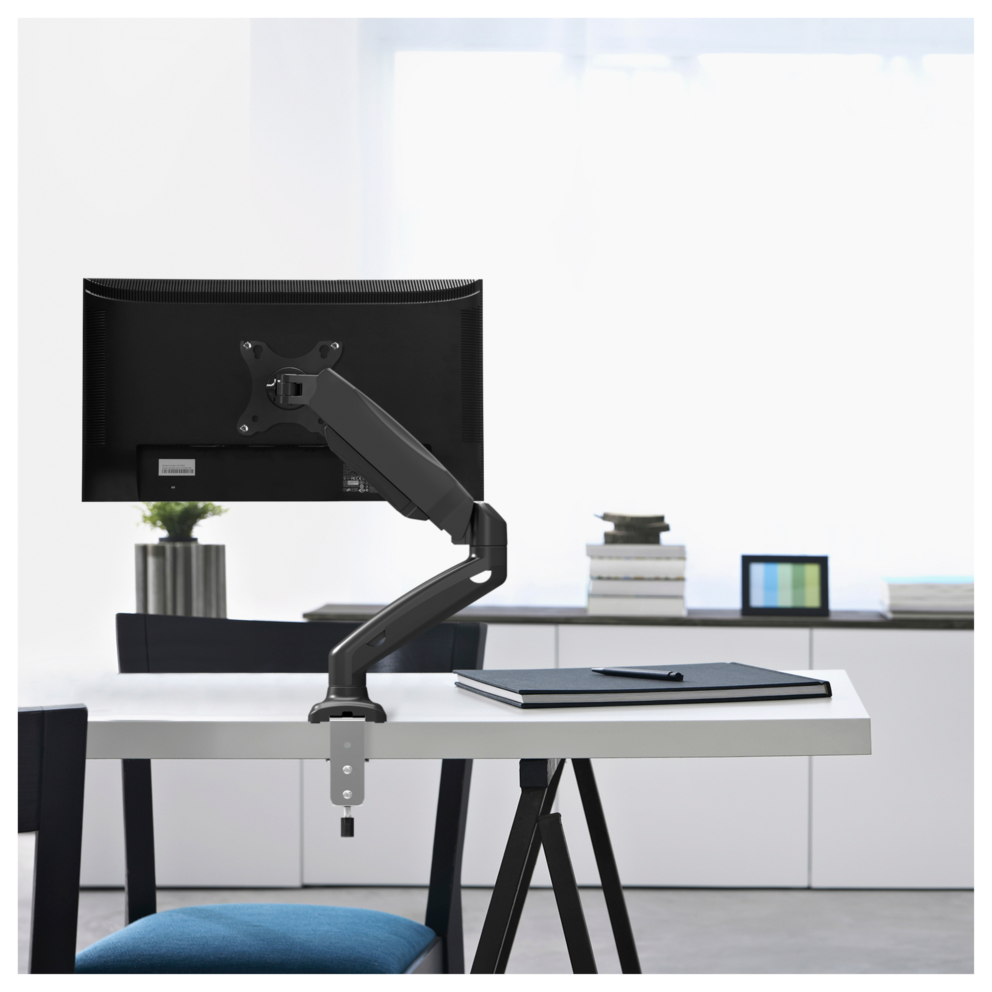 Monitor montado en un brazo articulado negro sobre un escritorio blanco con un cuaderno negro.