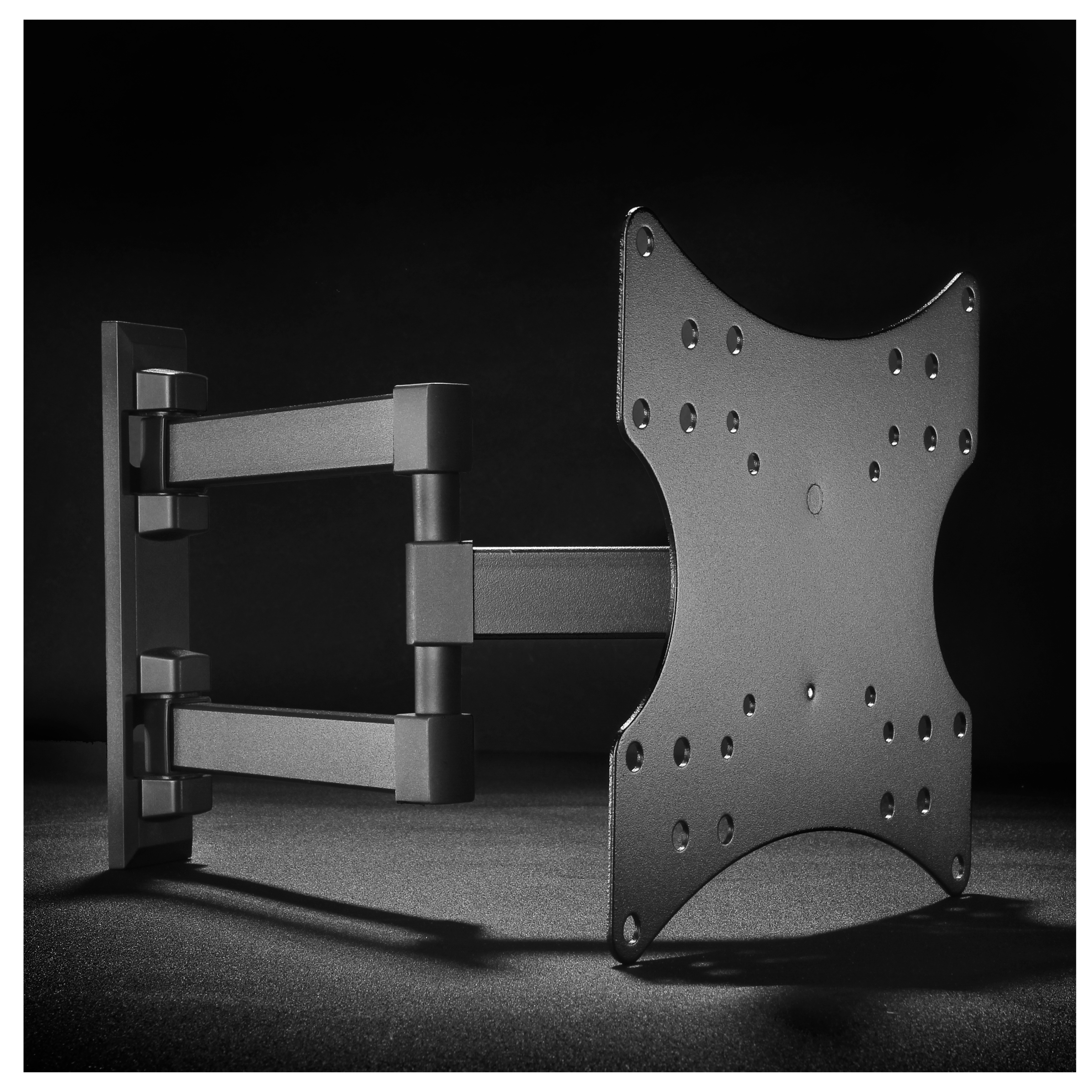 Soporte de TV negro y gris, con brazos ajustables, sobre una superficie gris oscuro. Fondo negro.
