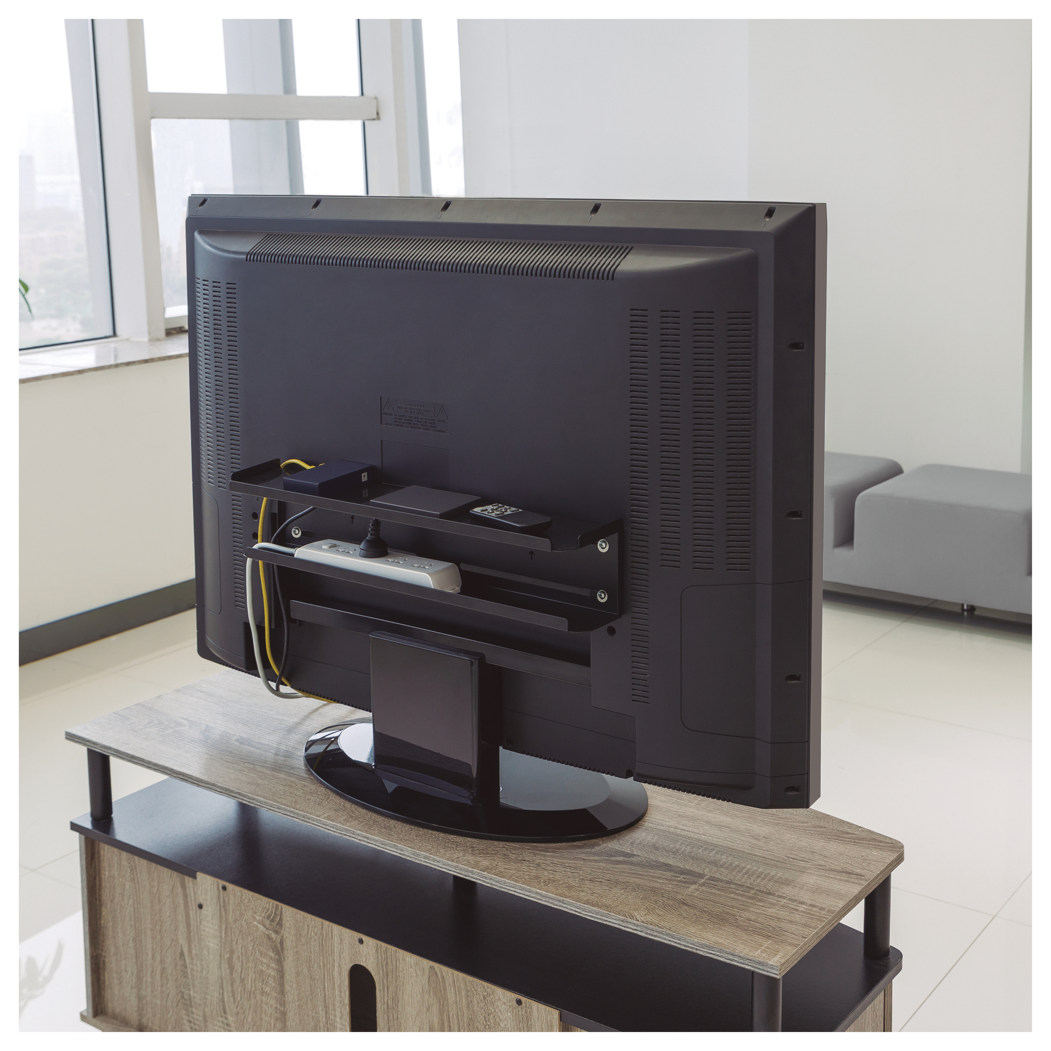 Parte trasera de un televisor negro montado en una pared. El televisor está sobre un mueble, con cables visibles.