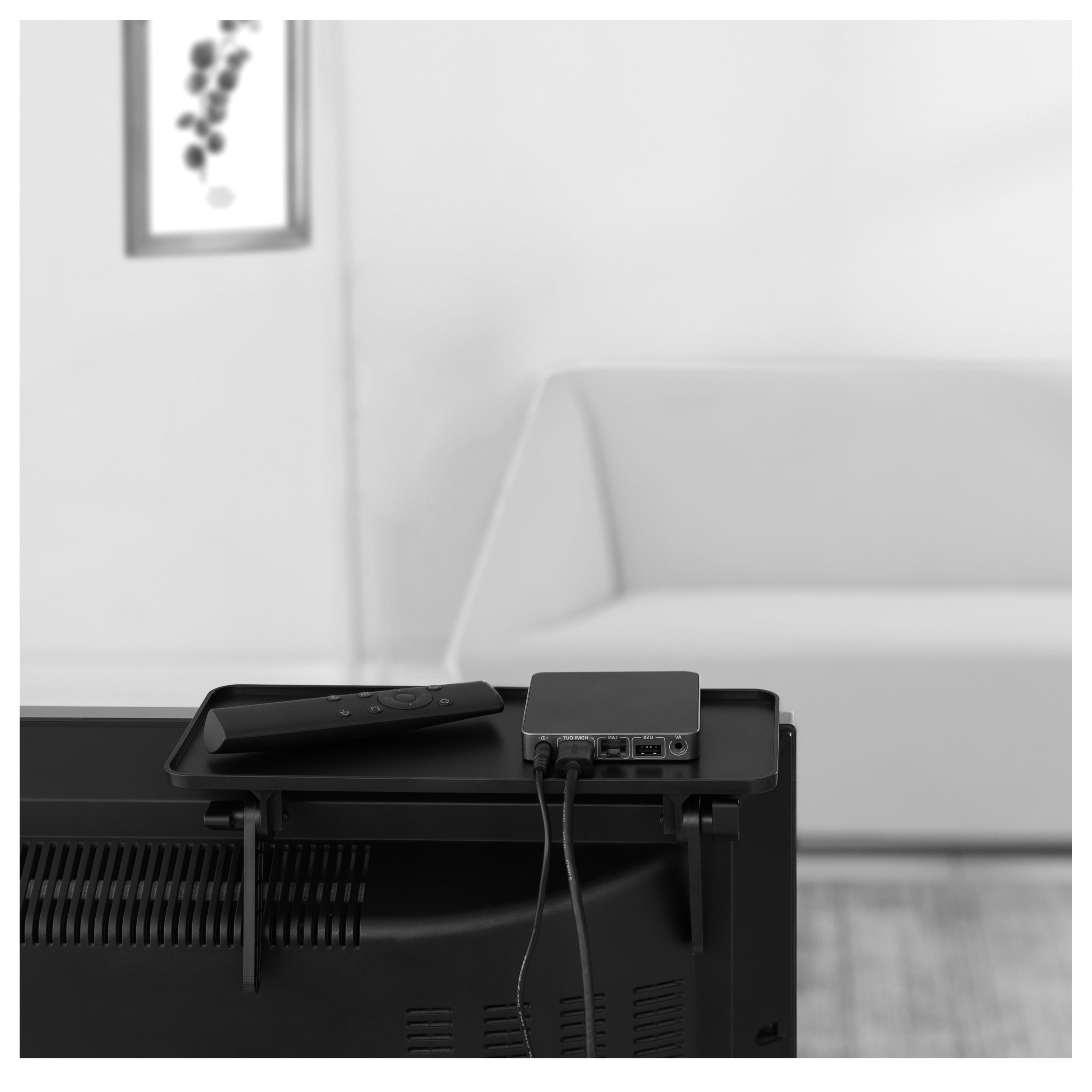 Una repisa negra con un dispositivo de transmisión y control remoto en un televisor. Sofá blanco atrás.