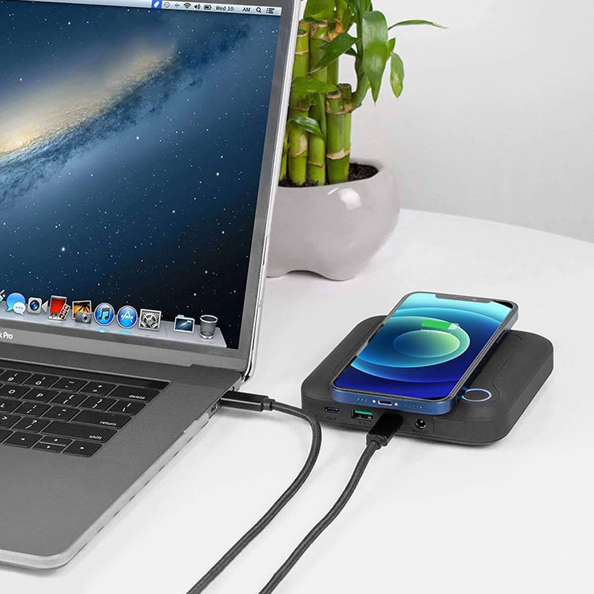 Ein Laptop, der mit einem Ladepad mit einem Telefon verbunden ist. Eine Pflanze ist im Hintergrund.