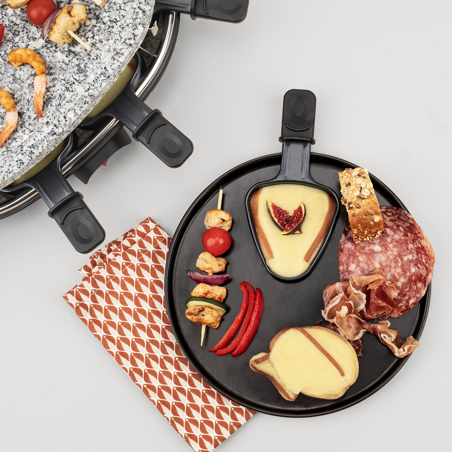 Raclette z jedzeniem na czarnym talerzu. Grillowane jedzenie i ser. Białe tło.