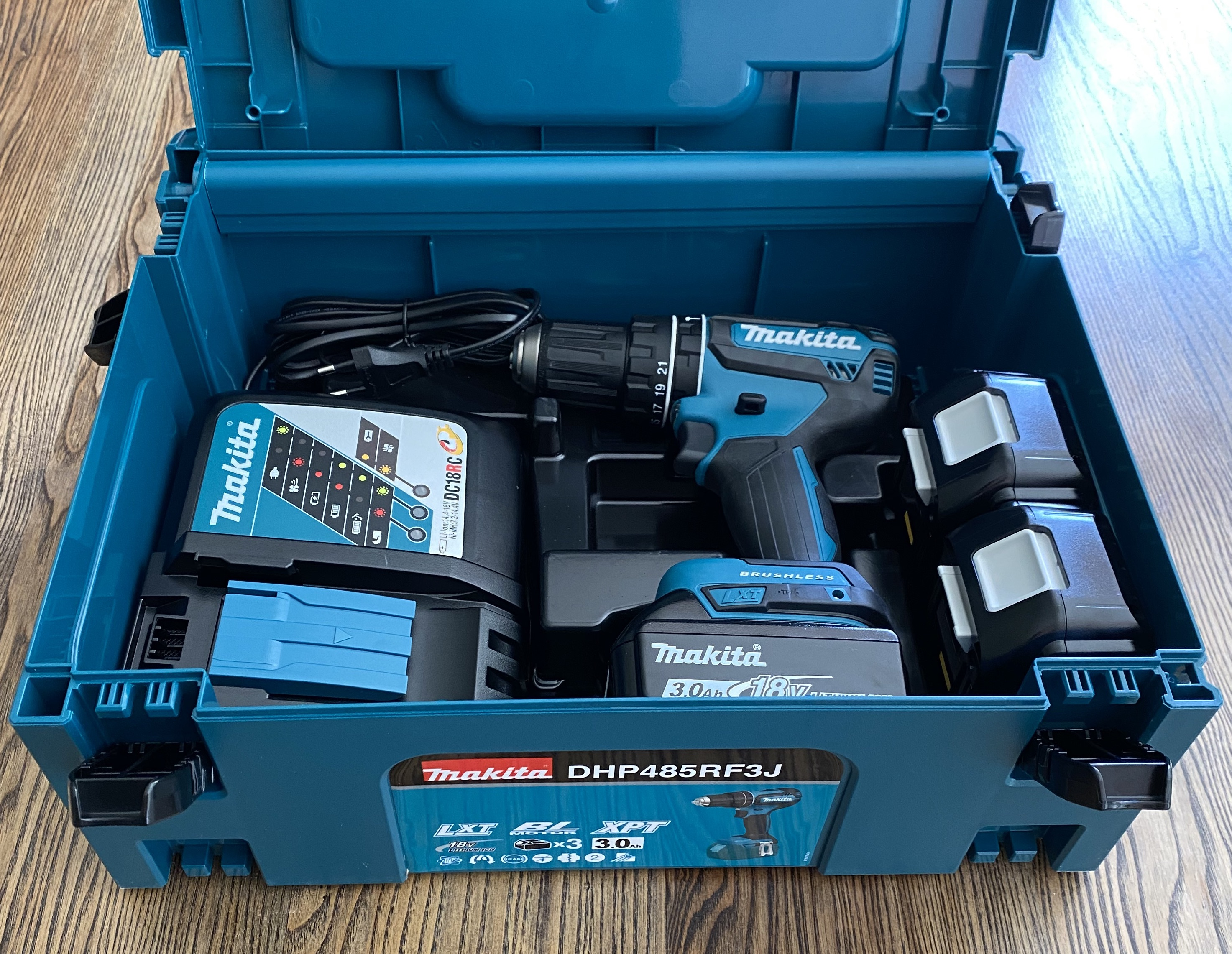 Offene türkisfarbene Werkzeugbox mit Bohrmaschine, Akkus und Ladegerät.