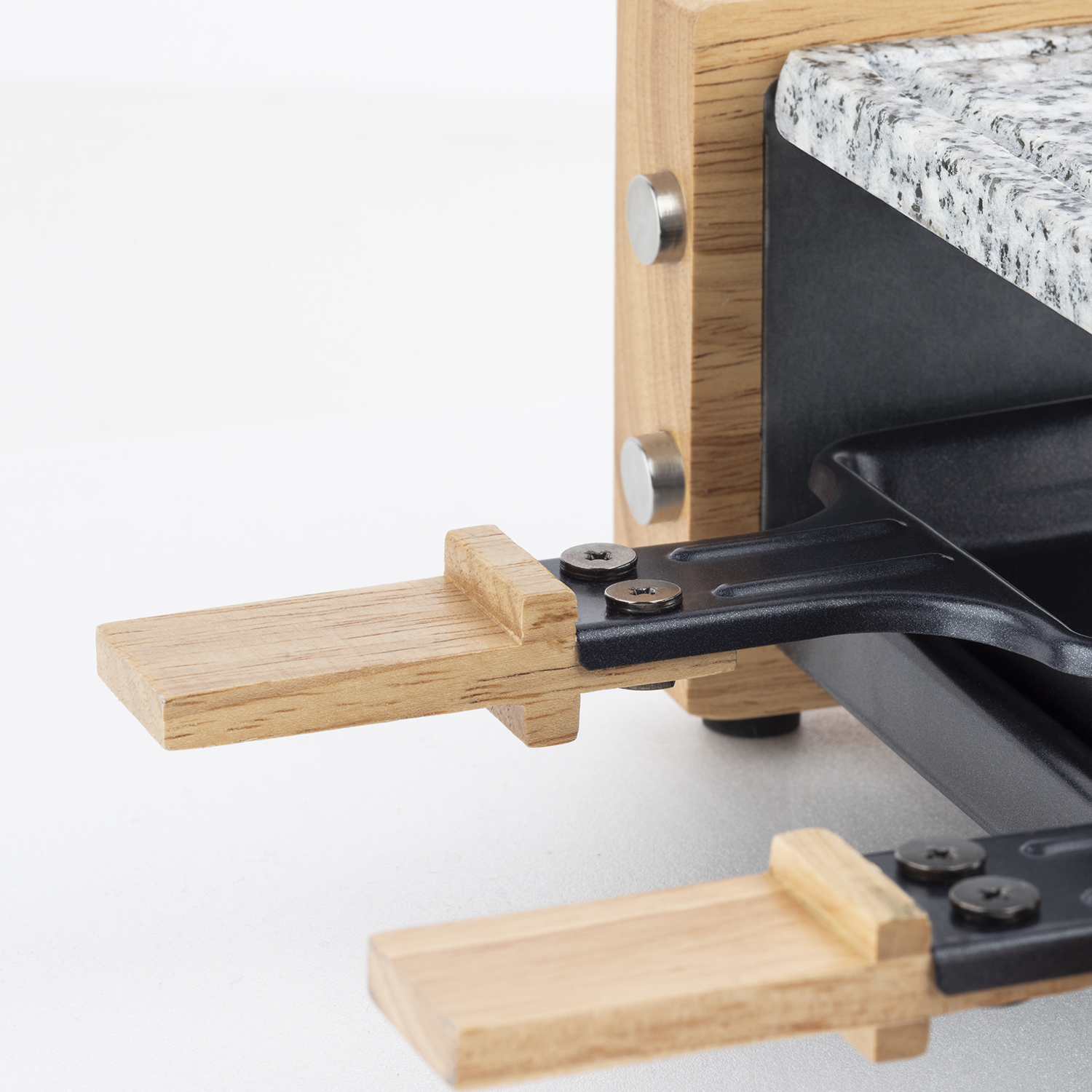 Zbliżenie grilla do raclette pokazujące drewniany uchwyt i kamień granitowy.