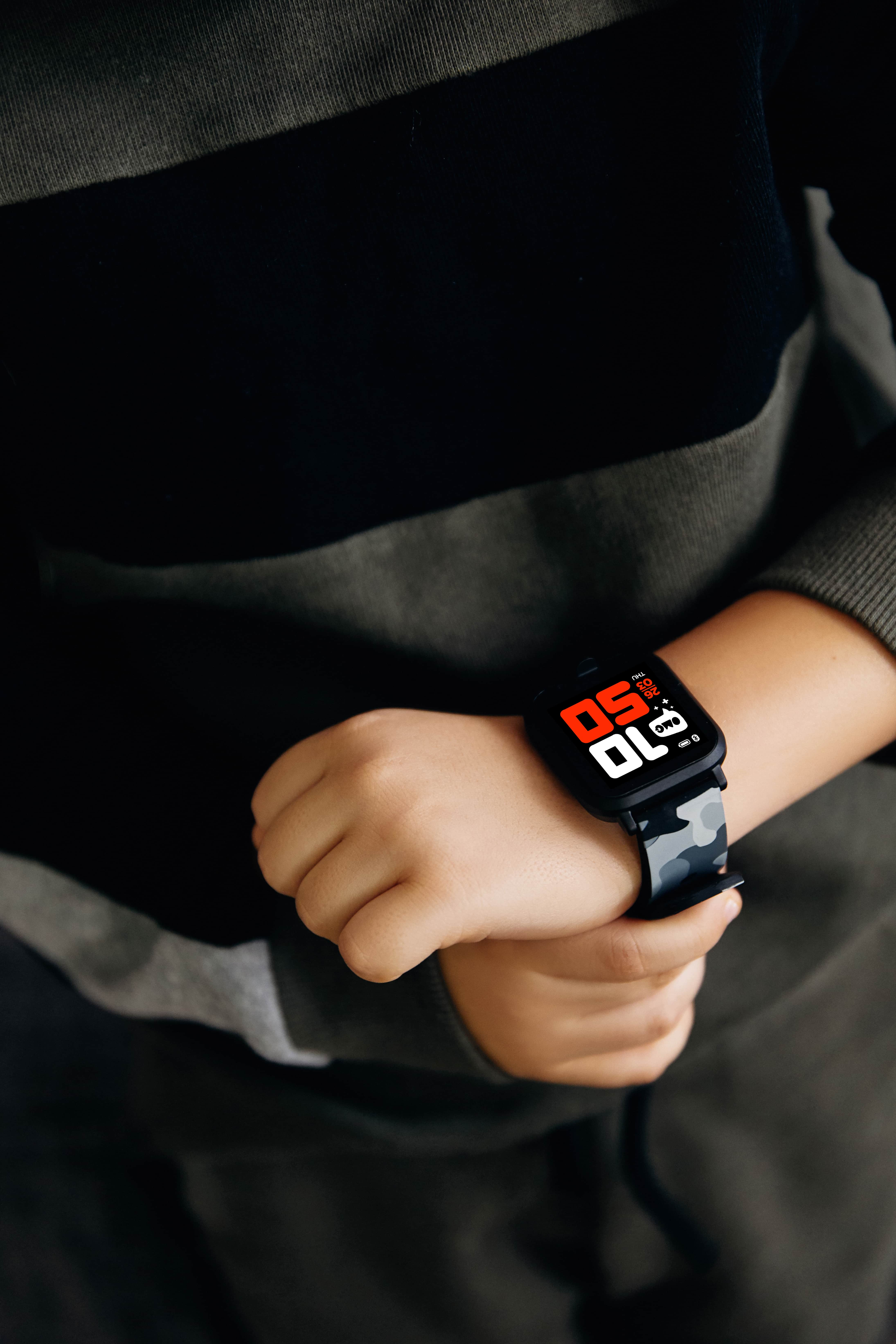 Muñeca de niño con smartwatch mostrando la hora y correa camuflada.