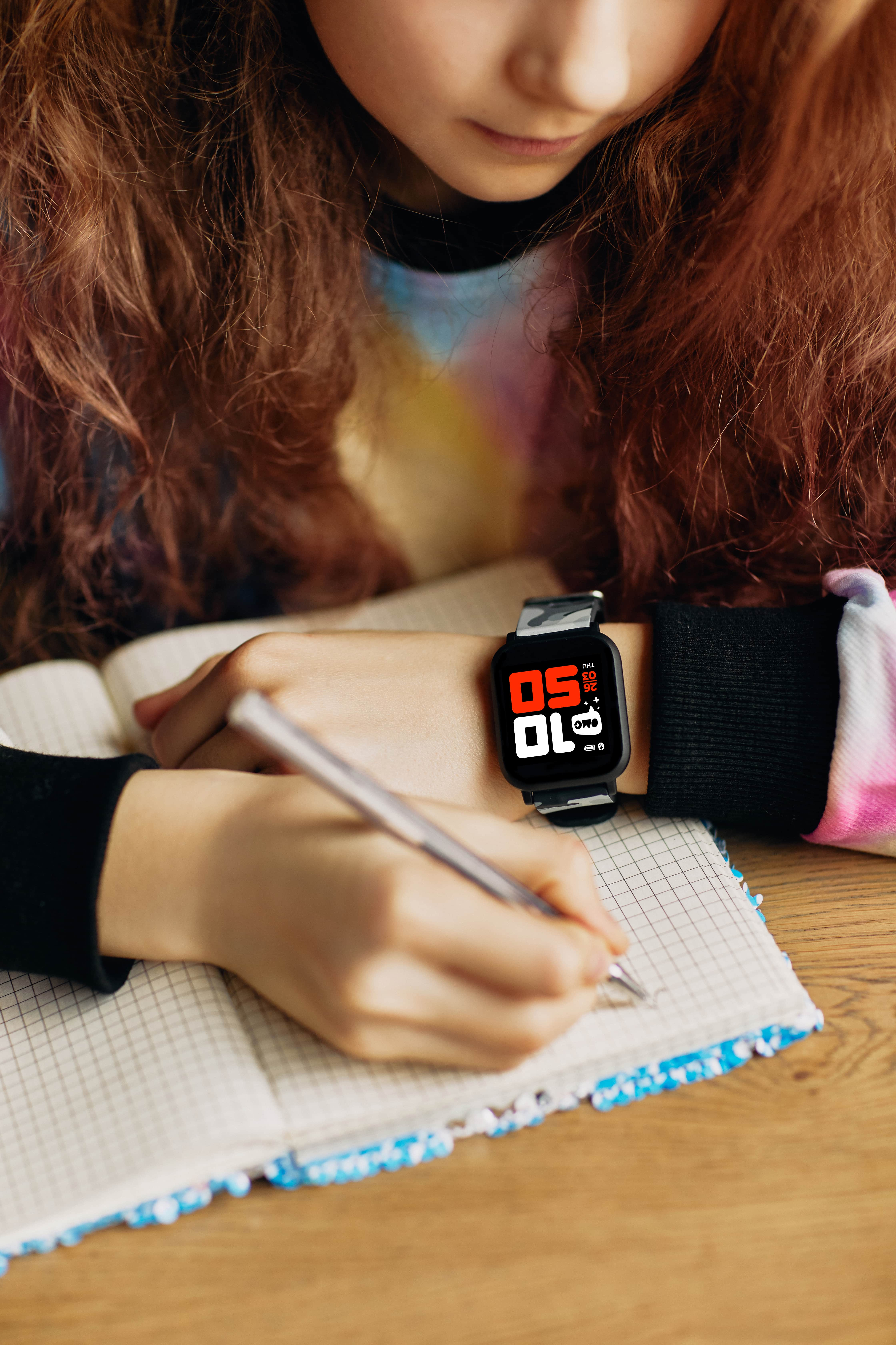 Una chica escribiendo en un bloc de notas, lleva un smartwatch en la muñeca.