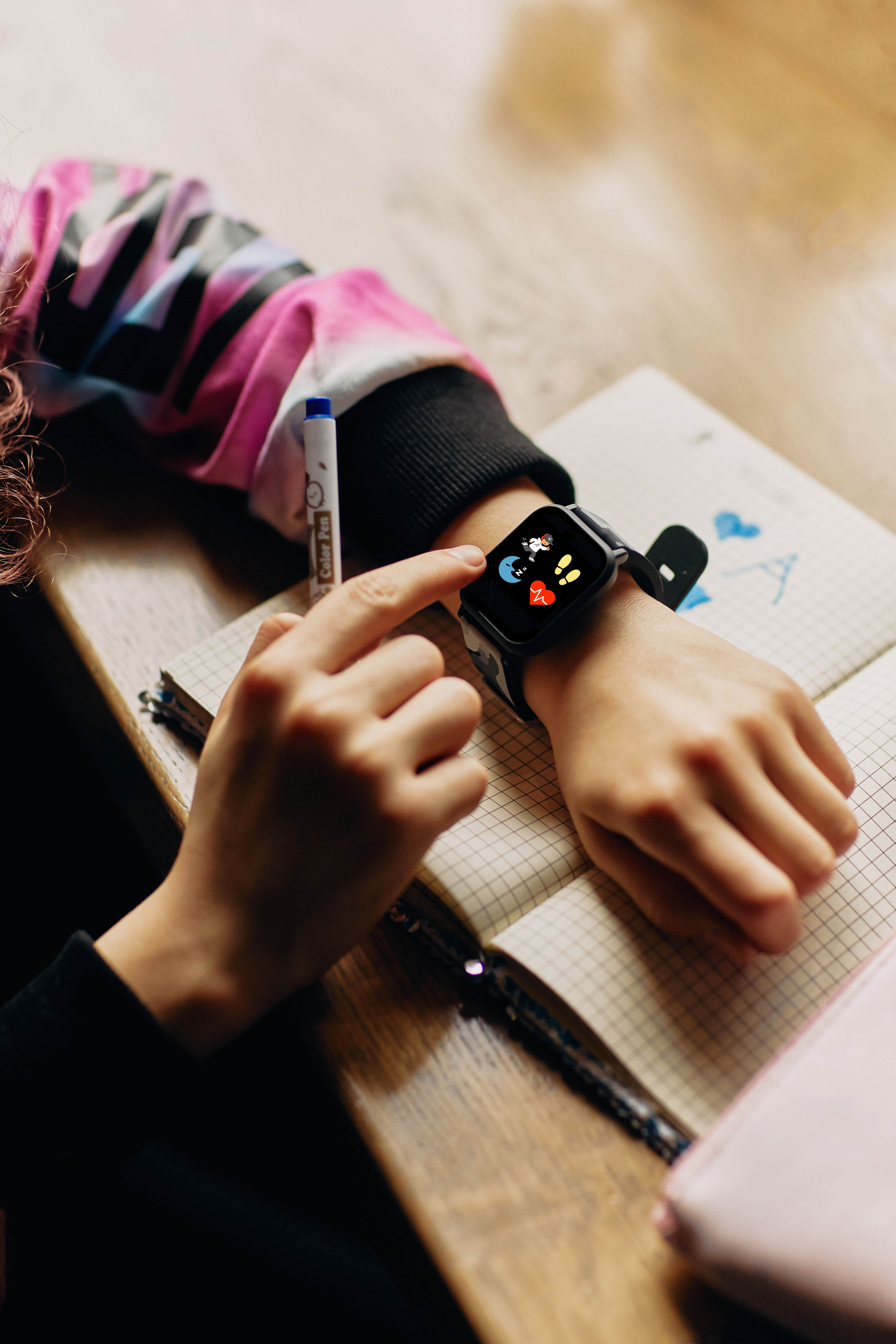La mano de un niño tocando un smartwatch con una pantalla colorida que muestra iconos en un escritorio.