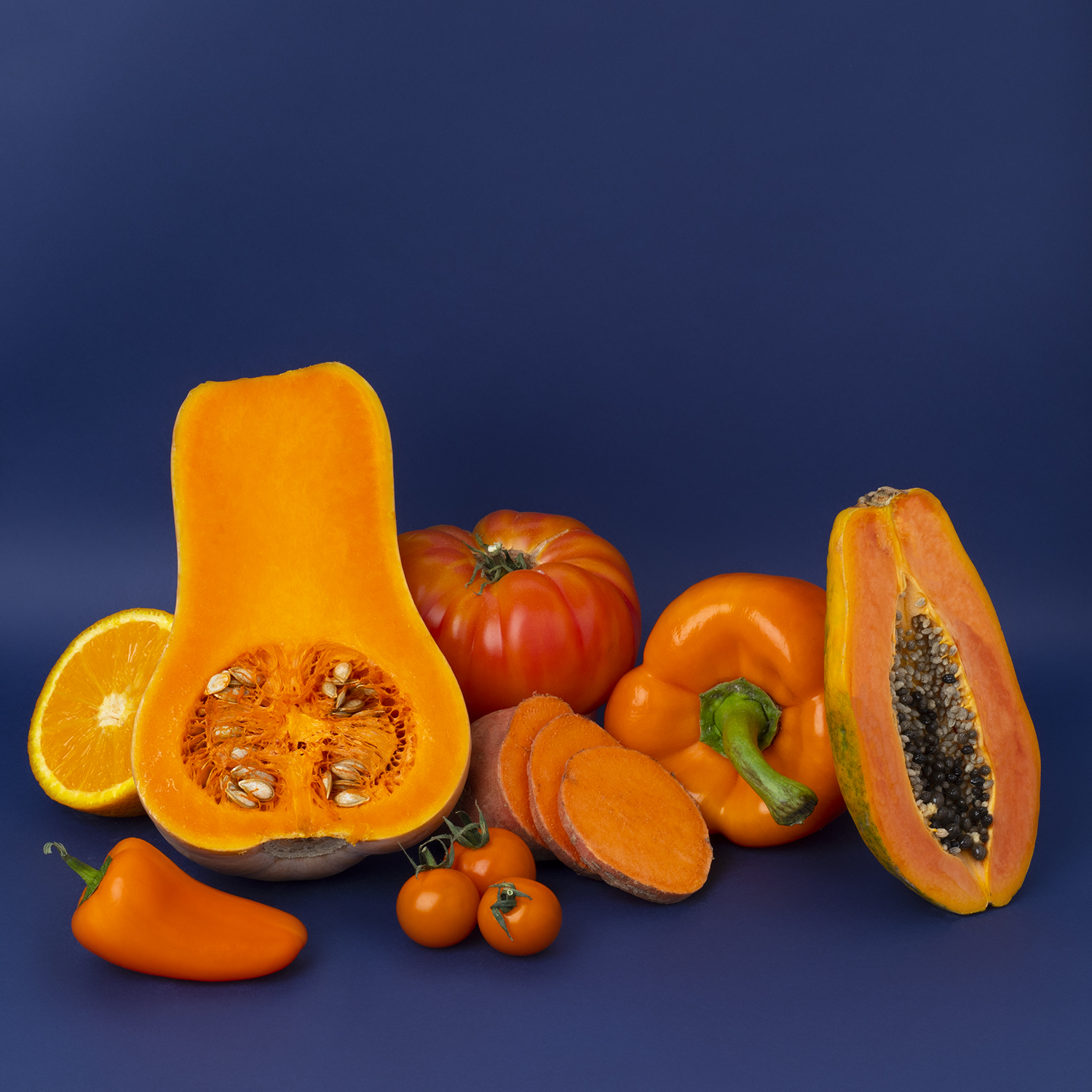 Assortimento di verdure arancioni su sfondo blu: zucca, arancia, pomodoro, patate dolci e peperone.