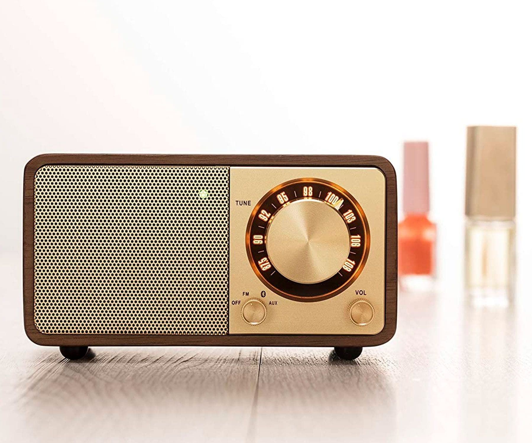 Drewniane radio retro ze złotymi akcentami i jasnozieloną tarczą. Butelki z lakierem do paznokci w tle.