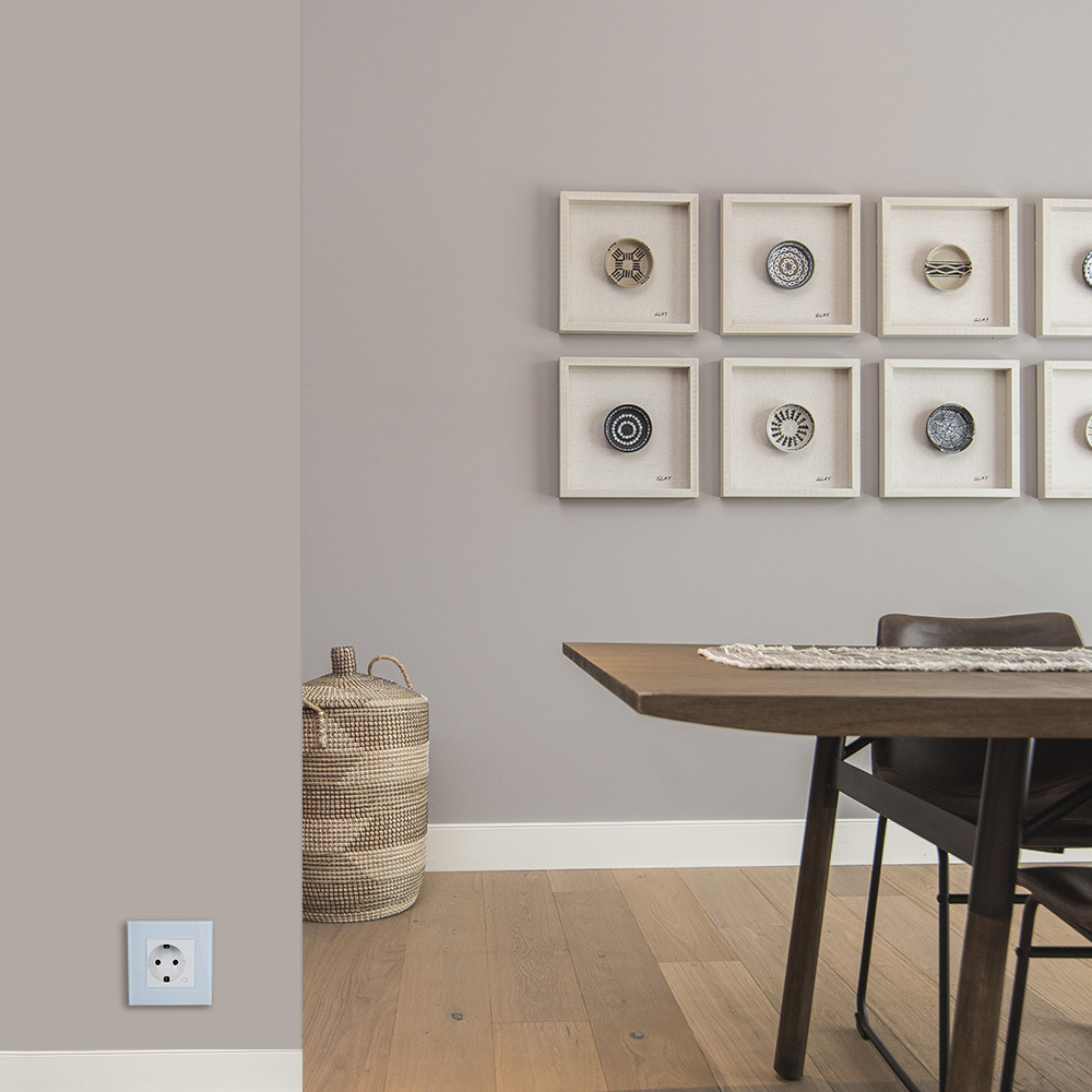 Pared con arte enmarcado y una cesta. Mesa y silla de madera al fondo.