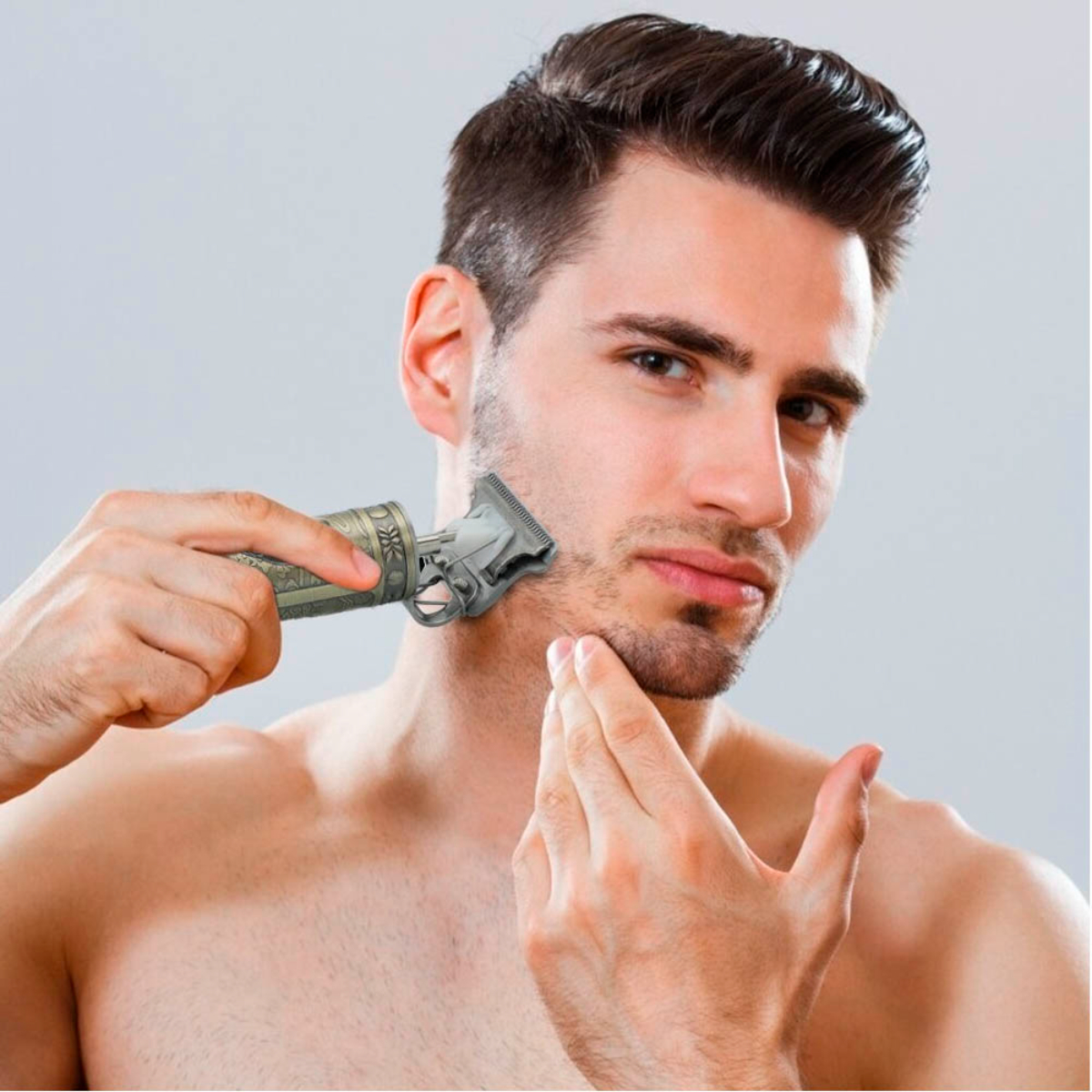 Un hombre se afeita la barba con una recortadora. Está sin camisa y mirando a la cámara.