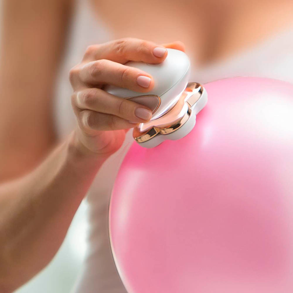 Una mujer afeita un globo rosa con una afeitadora eléctrica. La afeitadora es blanca y dorada.