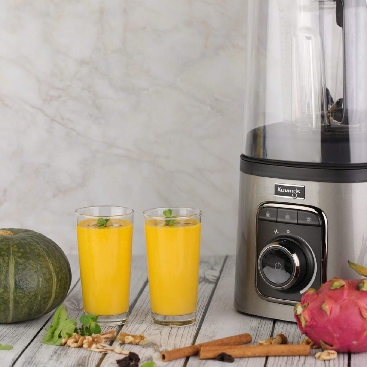 Dwie szklanki żółtego smoothie, blender, dynia, smoczy owoc, orzechy włoskie i cynamon.