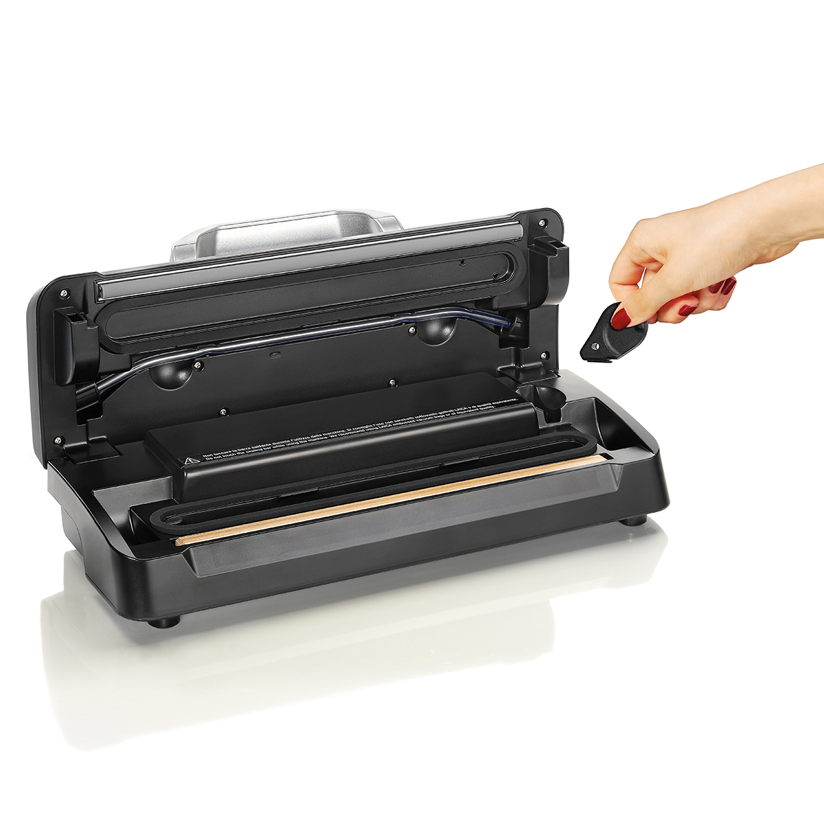 Ręka trzyma czarną, otwartą zgrzewarkę próżniową. Białe tło.