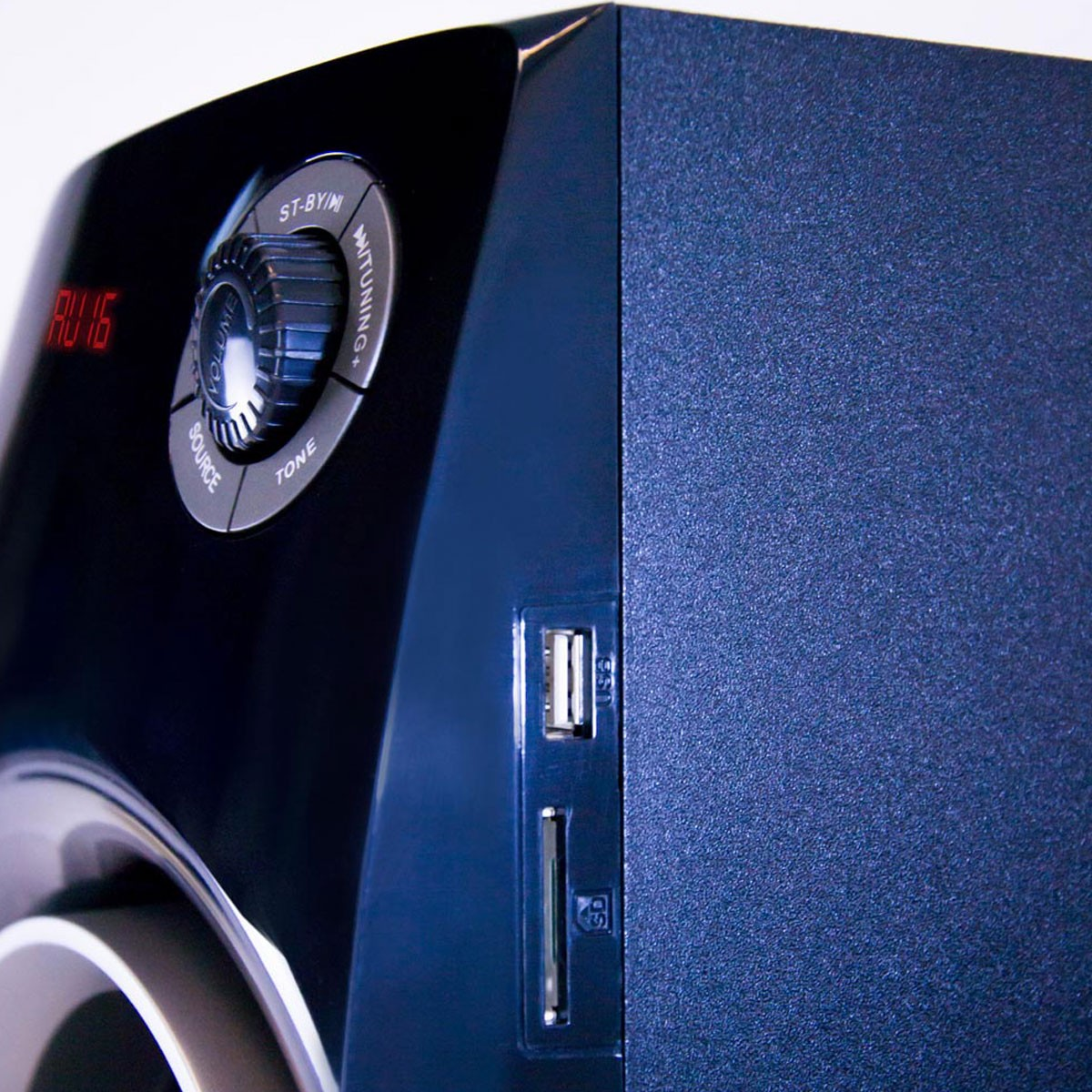 Altavoz negro y azul. Botones, pantalla con 'AU 16', puertos USB y tarjeta SD. Fondo blanco.