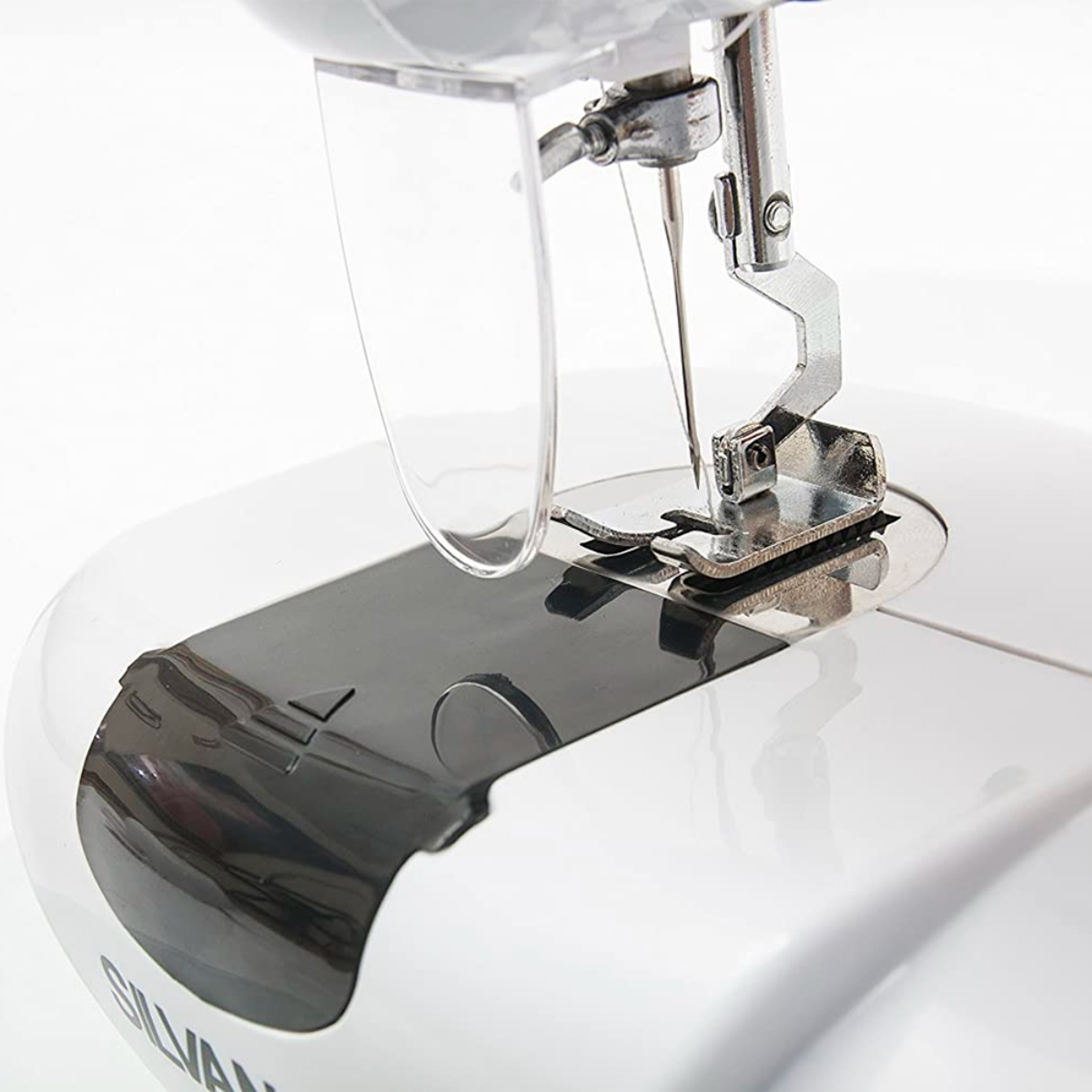 Primer plano de la aguja, el prensatelas y un protector de plástico transparente de una máquina de coser.