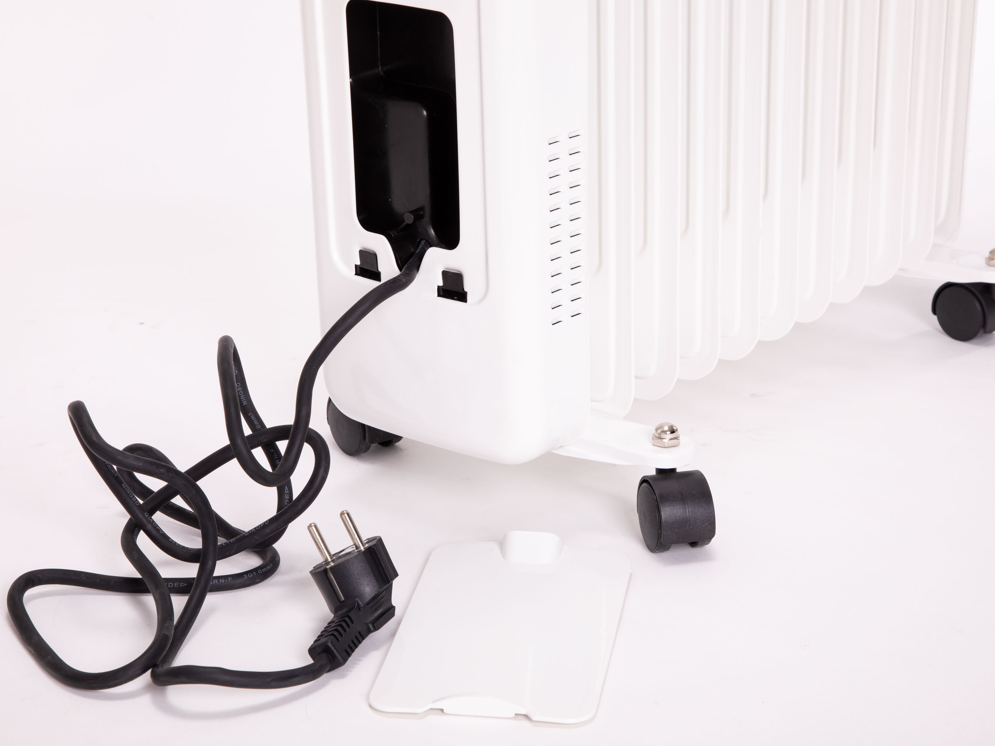 Weißer elektrischer Heizkörper mit schwarzem Kabel und Stecker, auf weißer Oberfläche. Ausgesteckt.