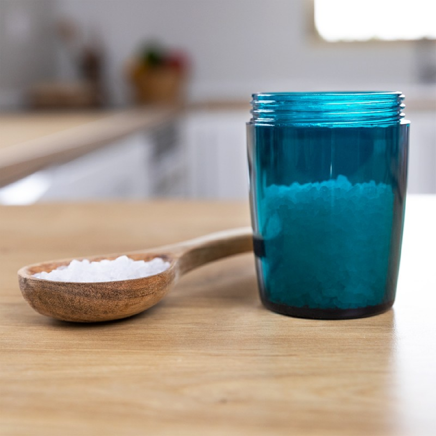 Een houten lepel met zout naast een blauwe glazen pot gevuld met zout op een houten oppervlak.