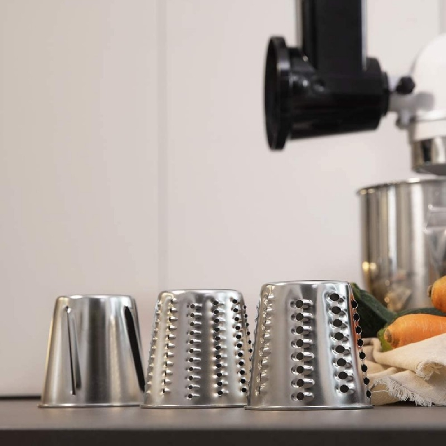 Trzy srebrne przystawki do robota kuchennego w stylu tarki na blacie kuchennym.