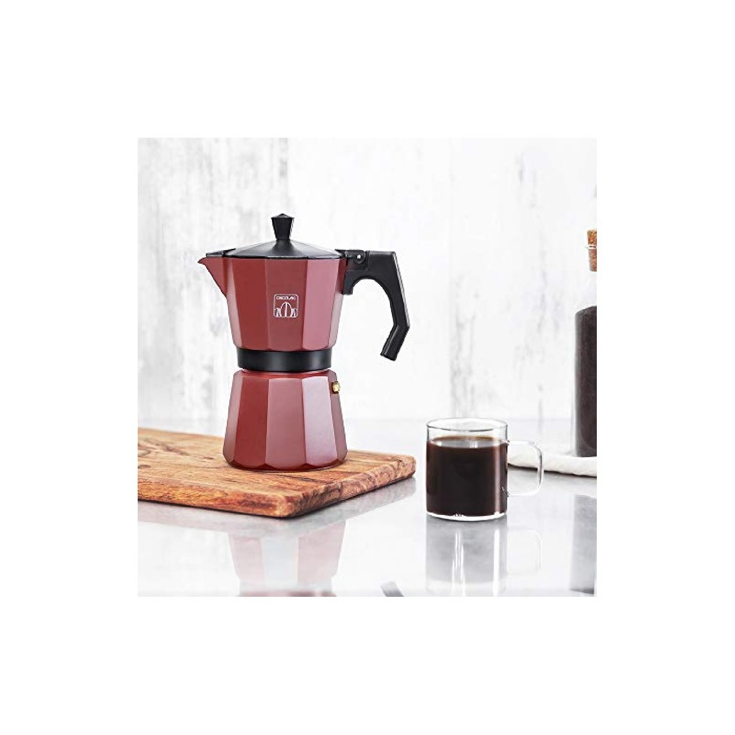 Cafetera roja con una taza de café sobre una tabla de madera, sobre fondo blanco.