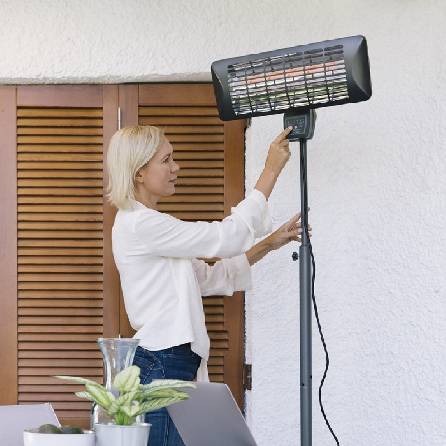 Kobieta reguluje grzejnik zewnętrzny na patio, w pobliżu stołu.