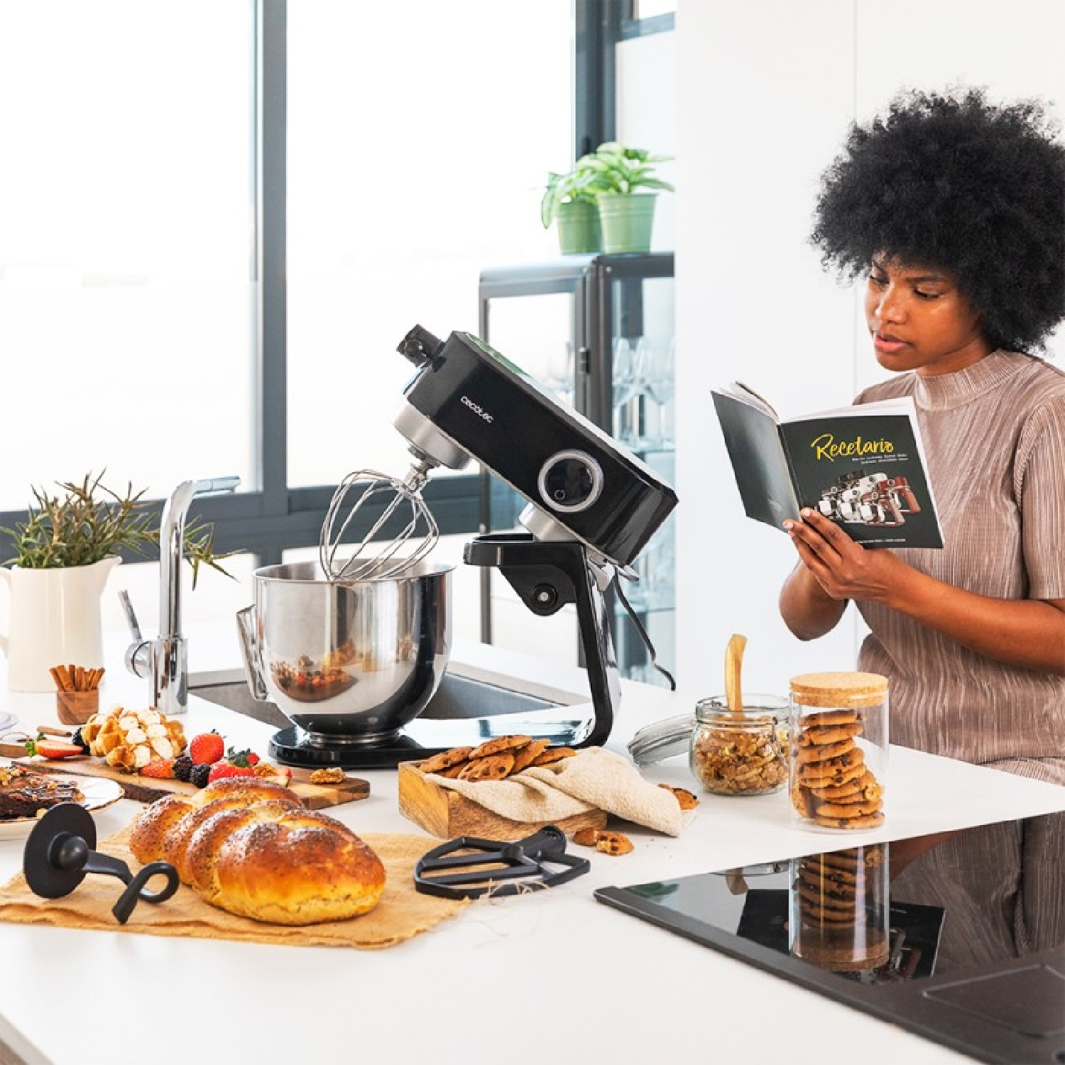 Donna legge un libro di cucina in cucina con un mixer e vari alimenti.
