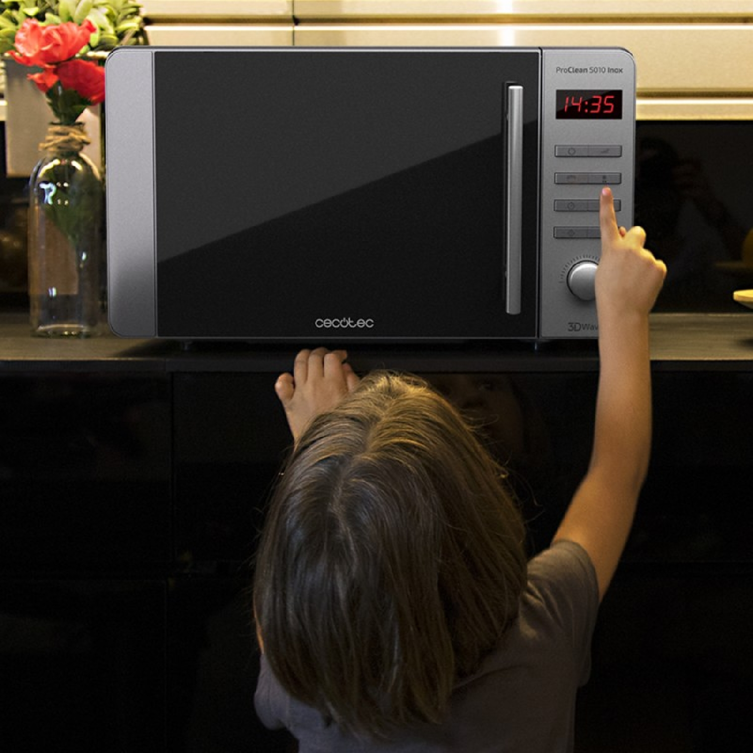 Un bambino che raggiunge un microonde sul bancone. Il microonde mostra '14:35'.