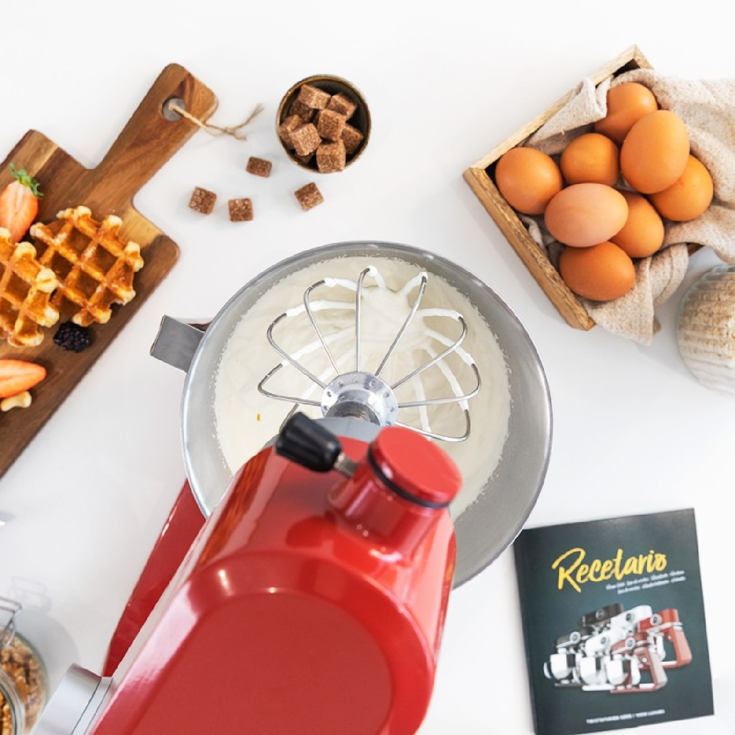 Robot da cucina rosso con ingredienti, tra cui uova, su sfondo bianco.