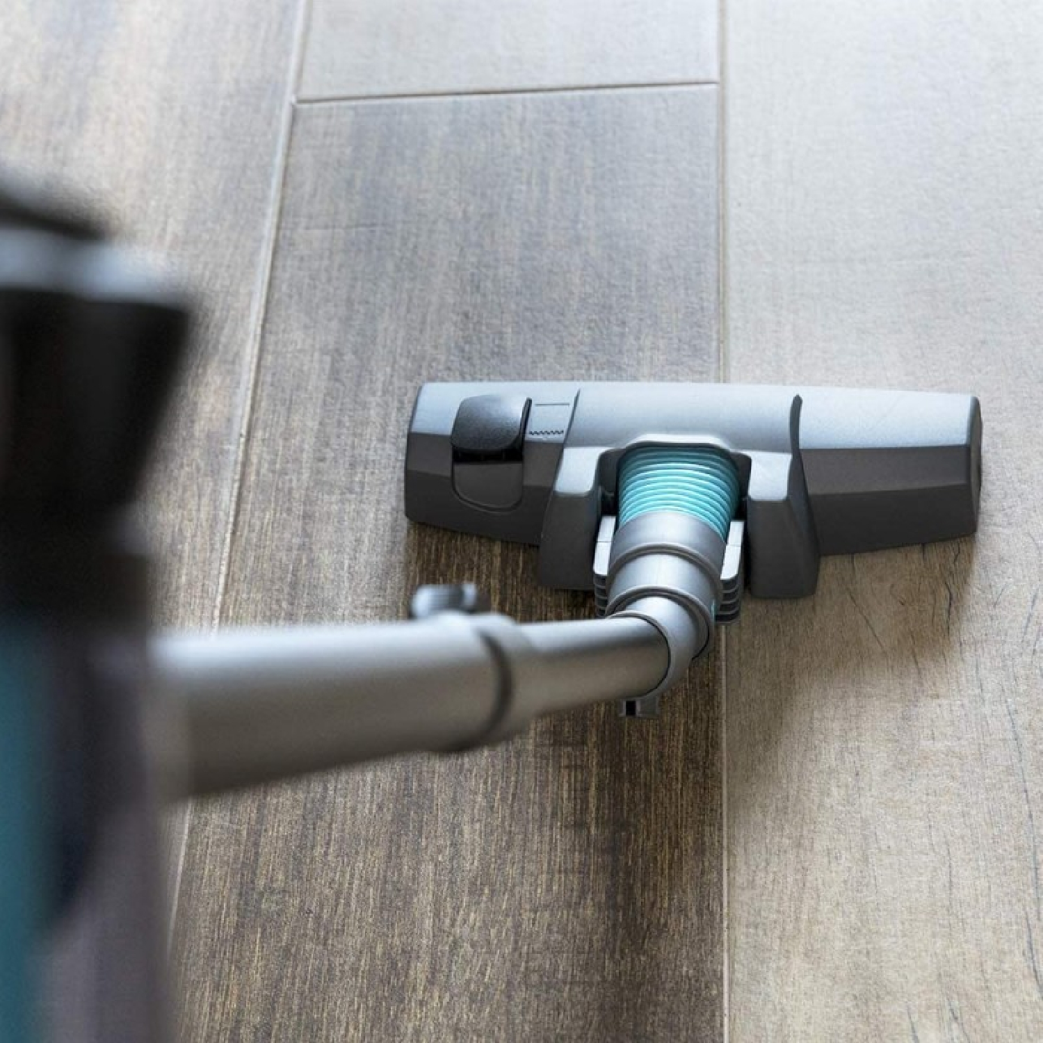 A vacuum cleaner head is on a wooden floor. The hose is in the top left corner of the image.