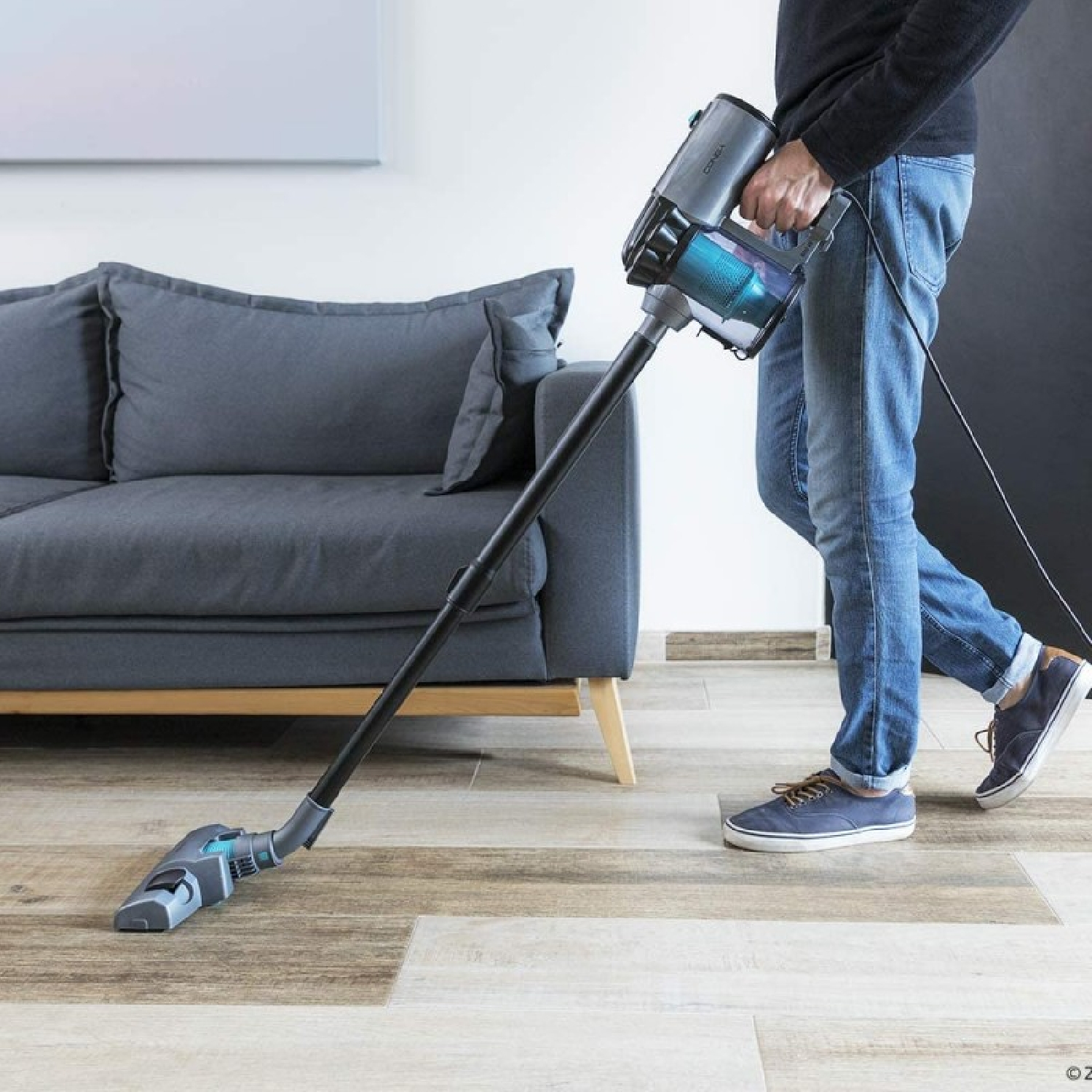A person vacuuming a room. They are using a black and gray vacuum cleaner.