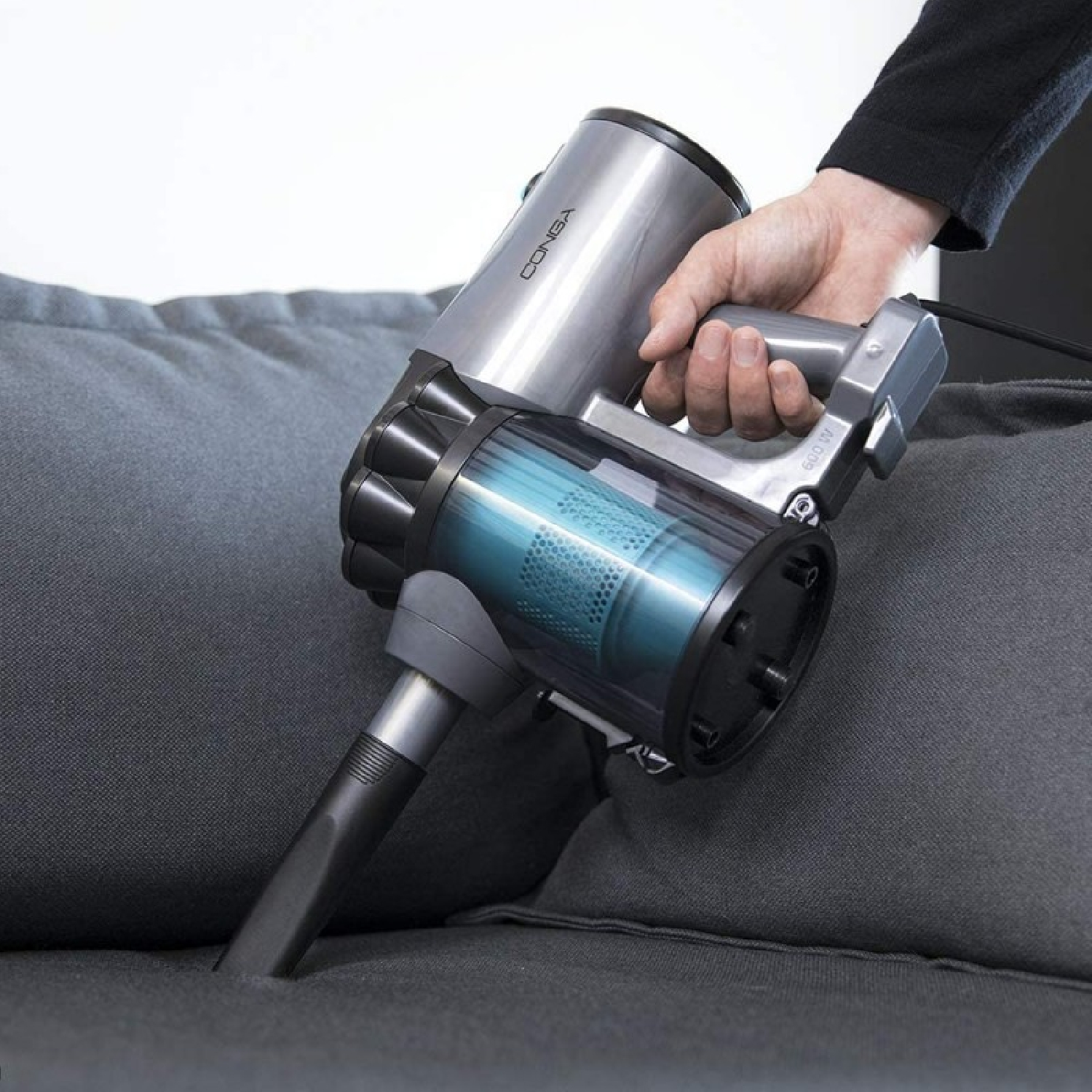 A person's hand using a handheld vacuum cleaner on a gray sofa.