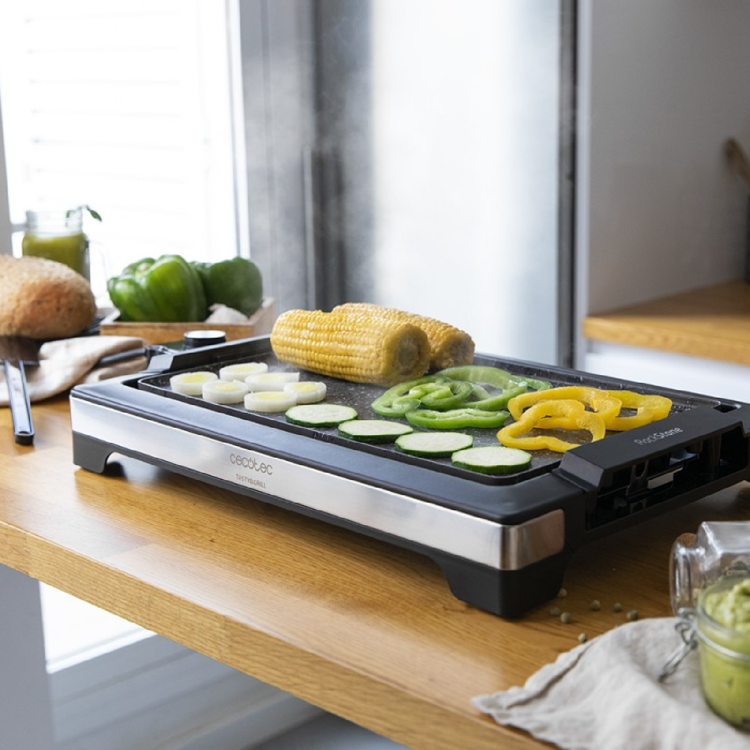 Elektrischer Grill mit geschnittenem Gemüse und Maiskolben. Es steht auf einer Holz-Arbeitsplatte.