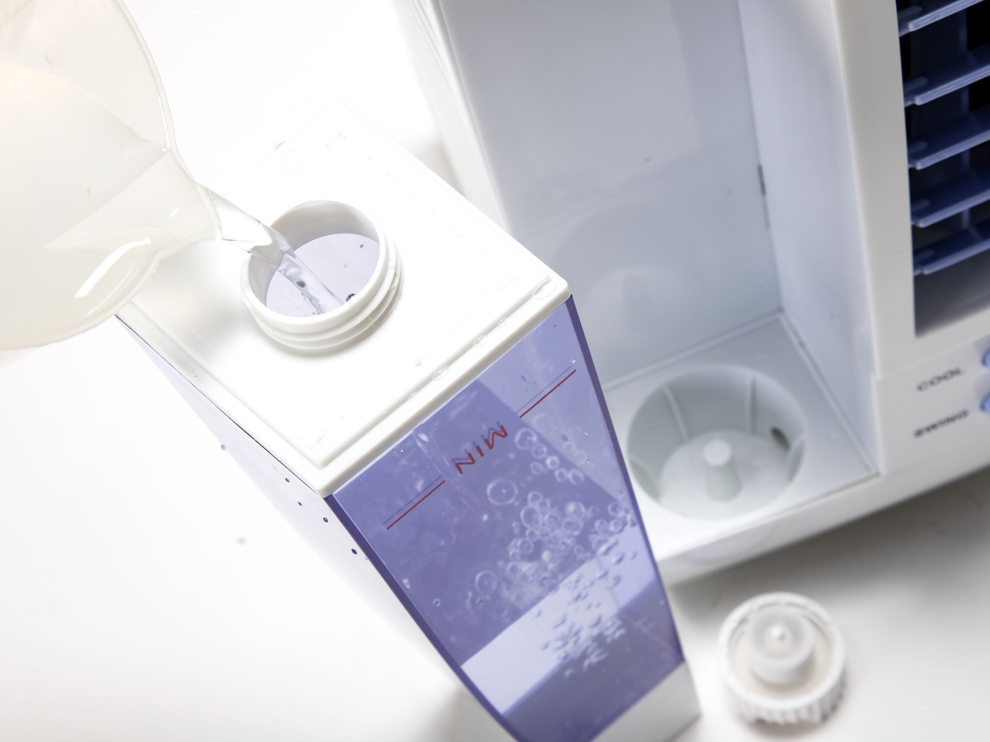 Agua vertiéndose en un tanque de agua blanco y morado. Tiene una marca de nivel mínimo.