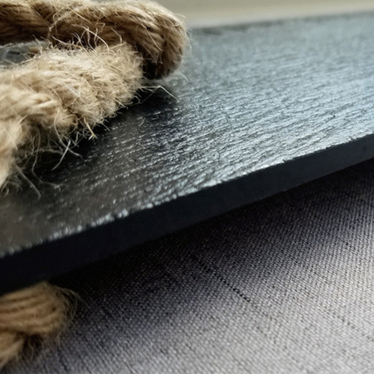 Primer plano de una pizarra negra con detalle de cuerda sobre una superficie gris.