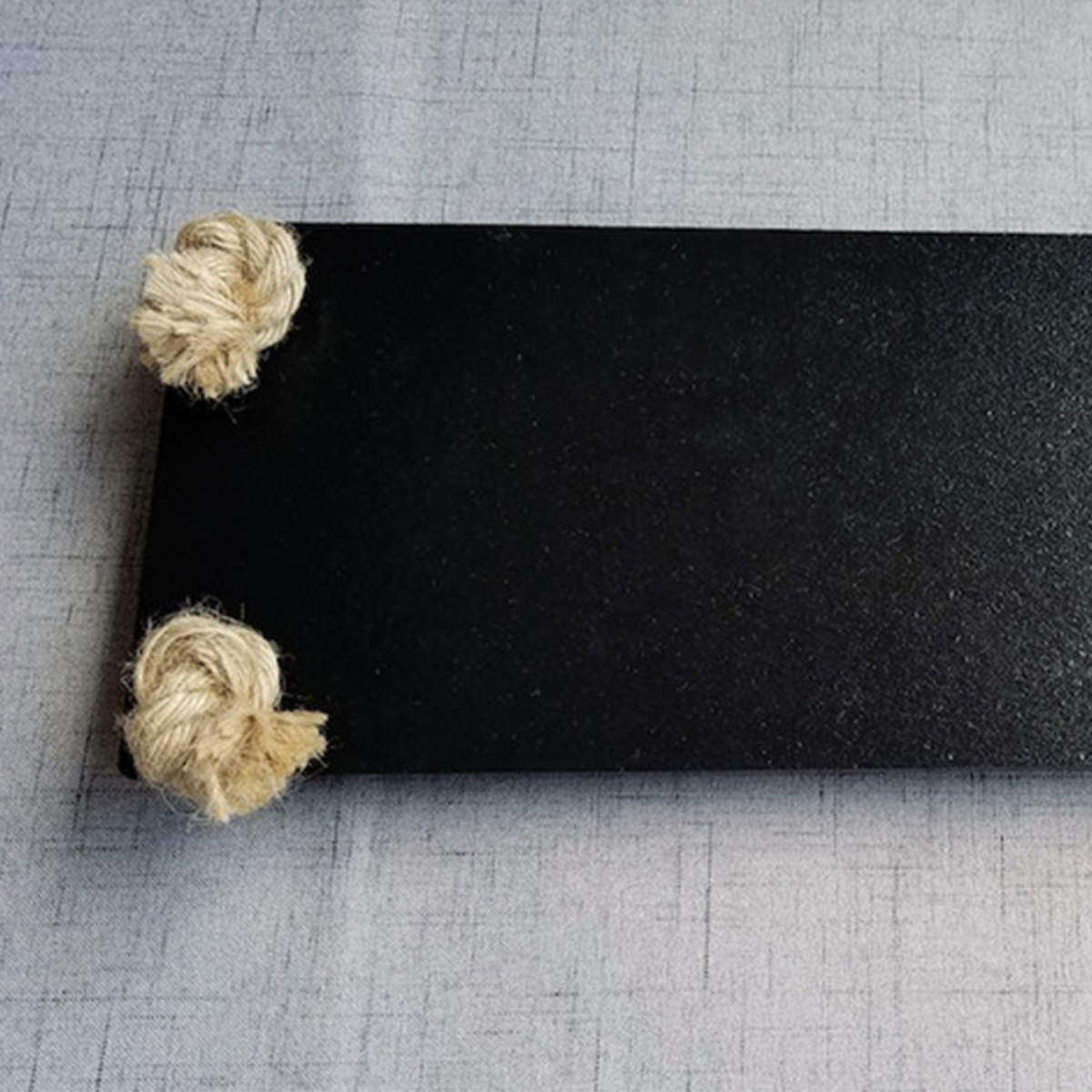 Estante de madera negro con nudos de cuerda sobre superficie gris. Diseño simple.