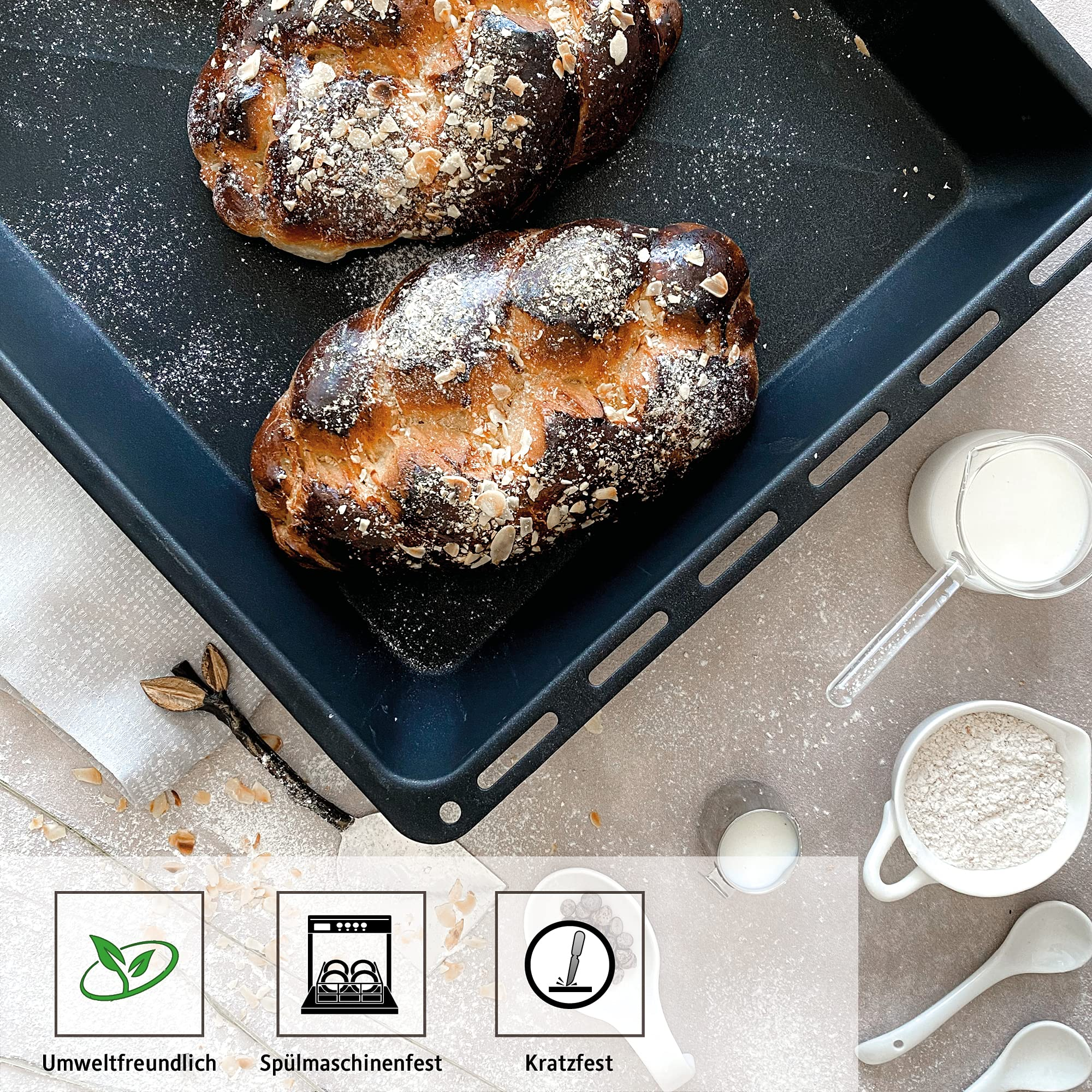 Zwei gebackene Brötchen auf einem schwarzen Backblech. Weißes Pulver ist darüber gestreut.